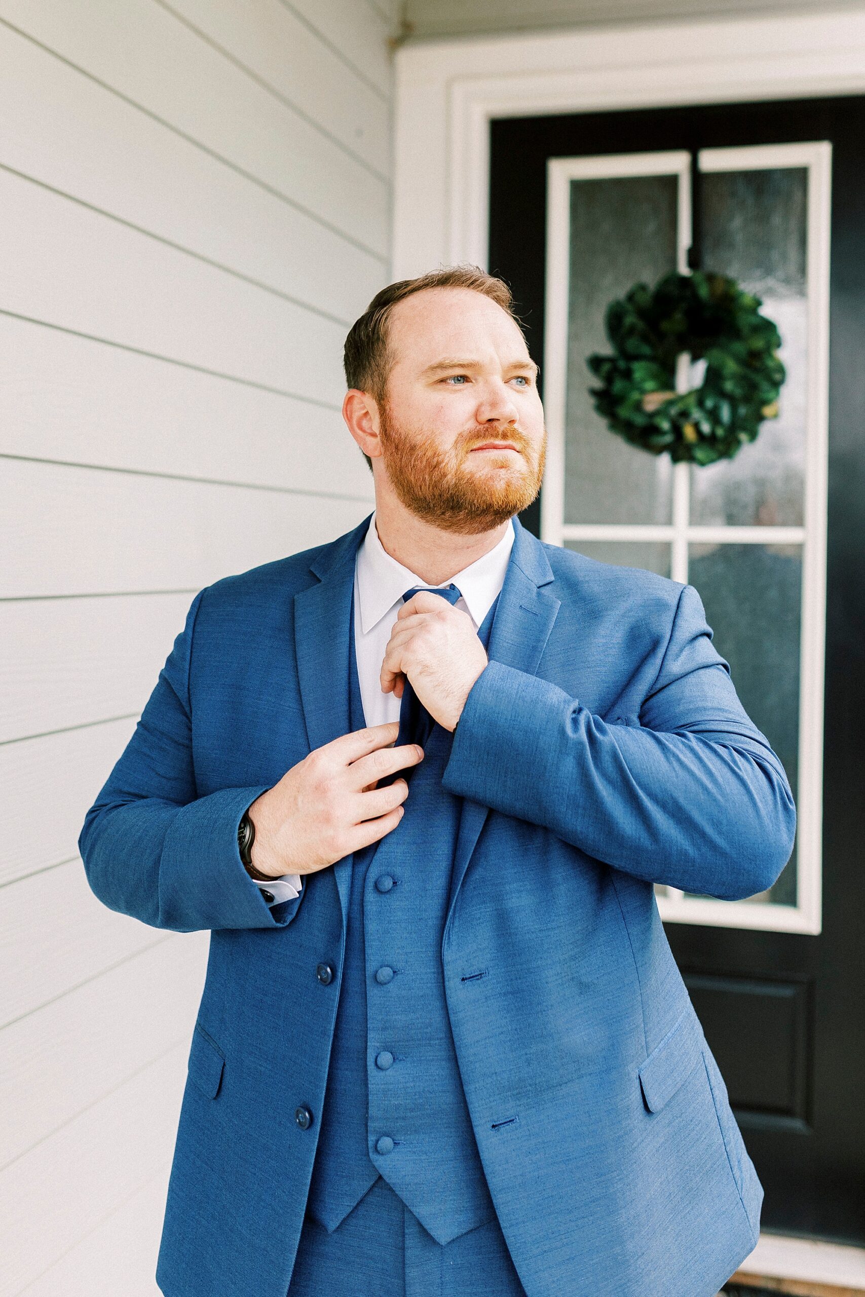 groom adjusts blue tie in front of front door before Downtown Kannapolis wedding