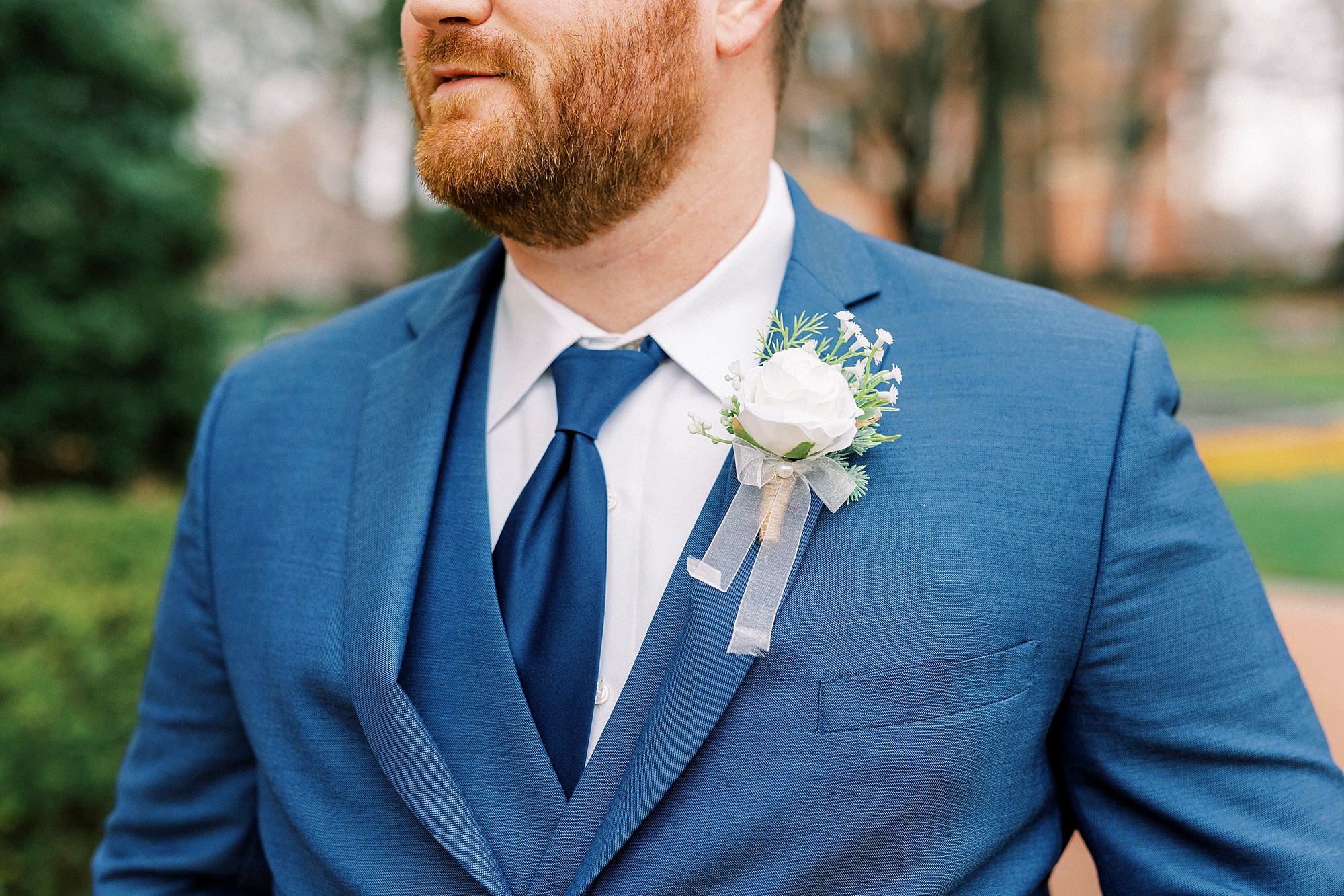 groom stands with white flower on lapel of blue suit