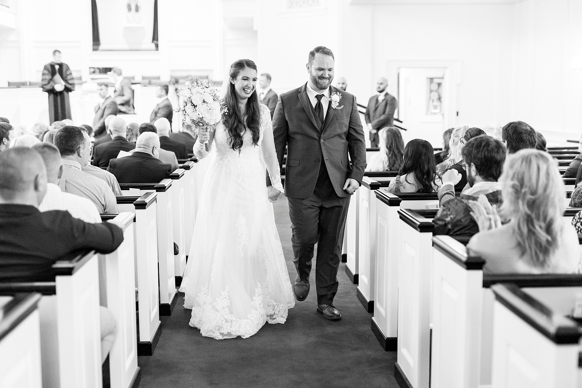 bride and groom hold hands walking up aisle after ceremony inside First Baptist Church in Kannapolis NC