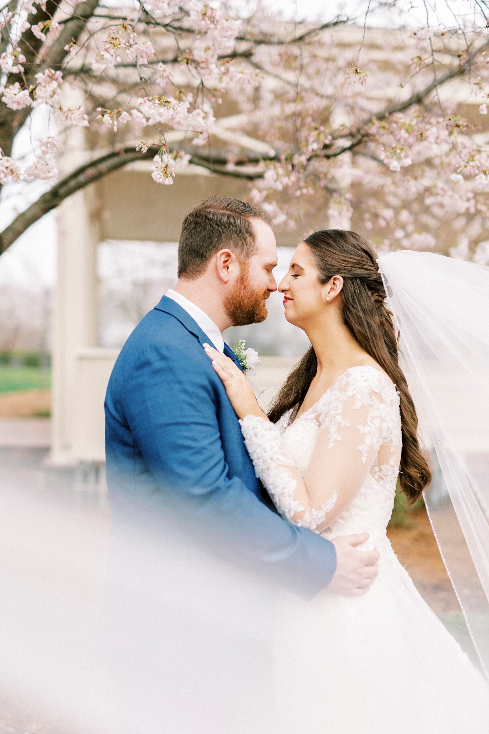 bride and groom lean heads together nuzzling noses under pink blossoms