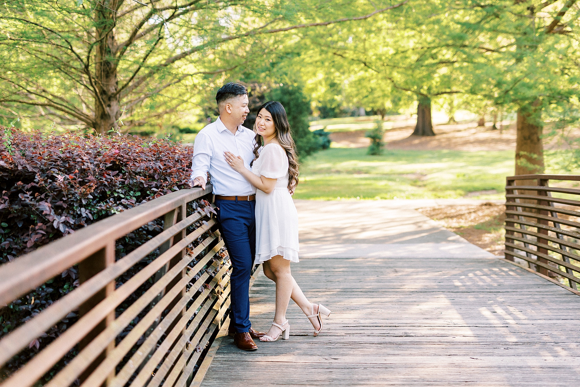 couple hugs against railing of bridge inside Glencairn Garden