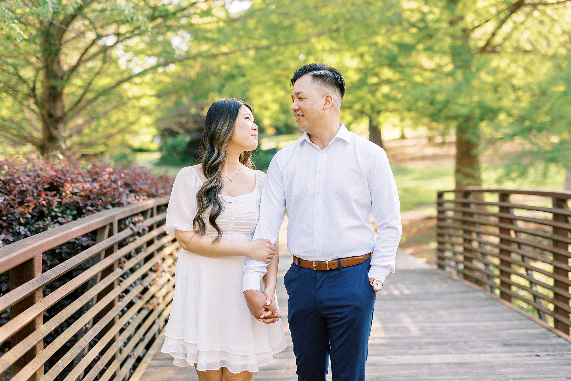 man and woman hold hands walking across bridge in Glencairn Garden