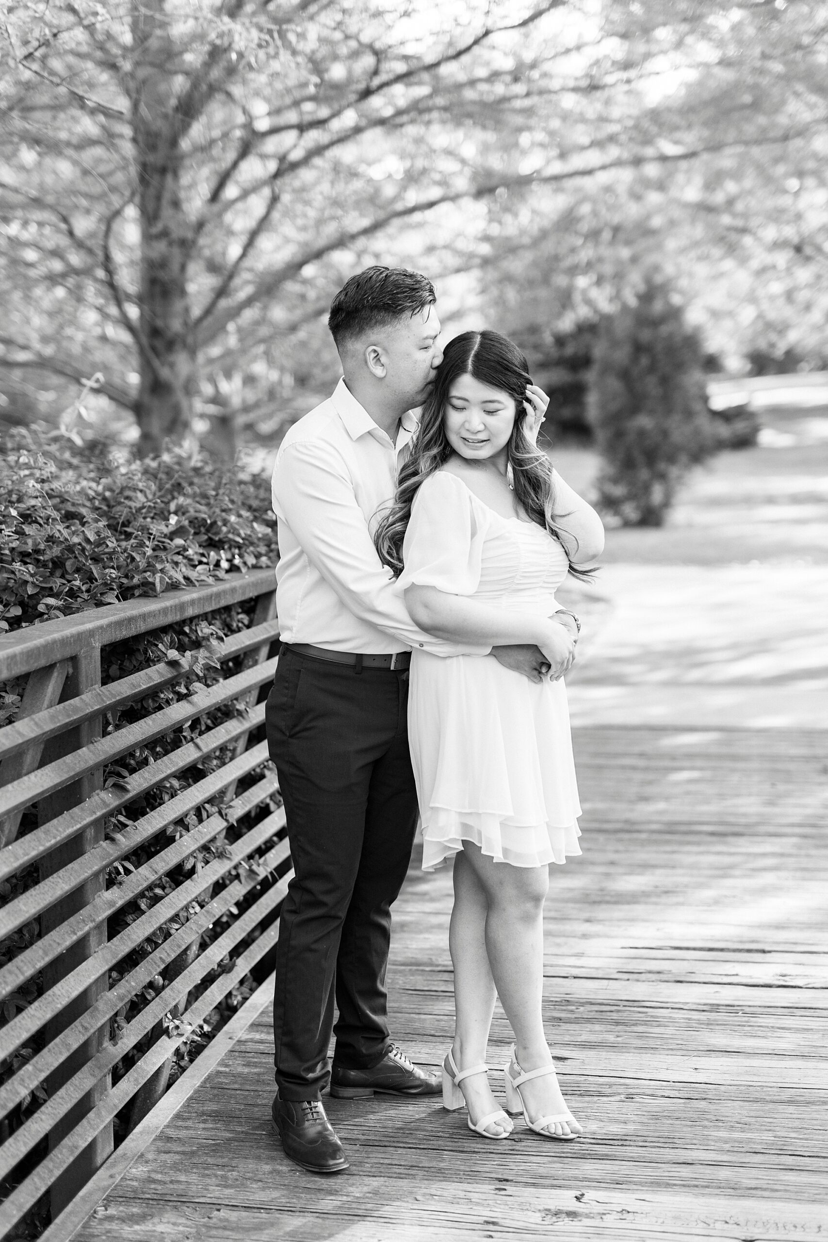 woman pushes her hair over her ear while man hugs from behind 