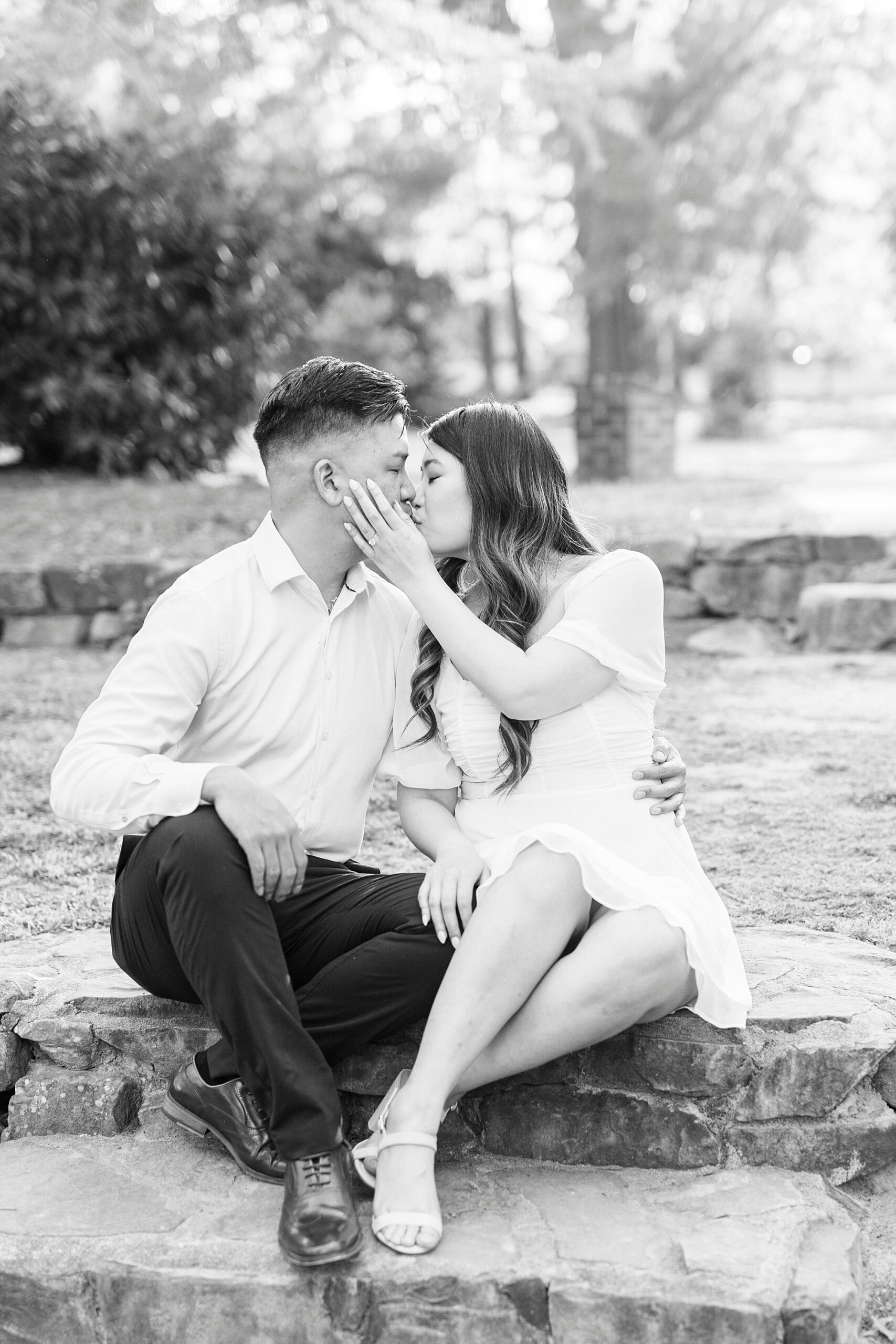 woman leans to kiss man sitting on staircase in the grass at Glencairn Garden