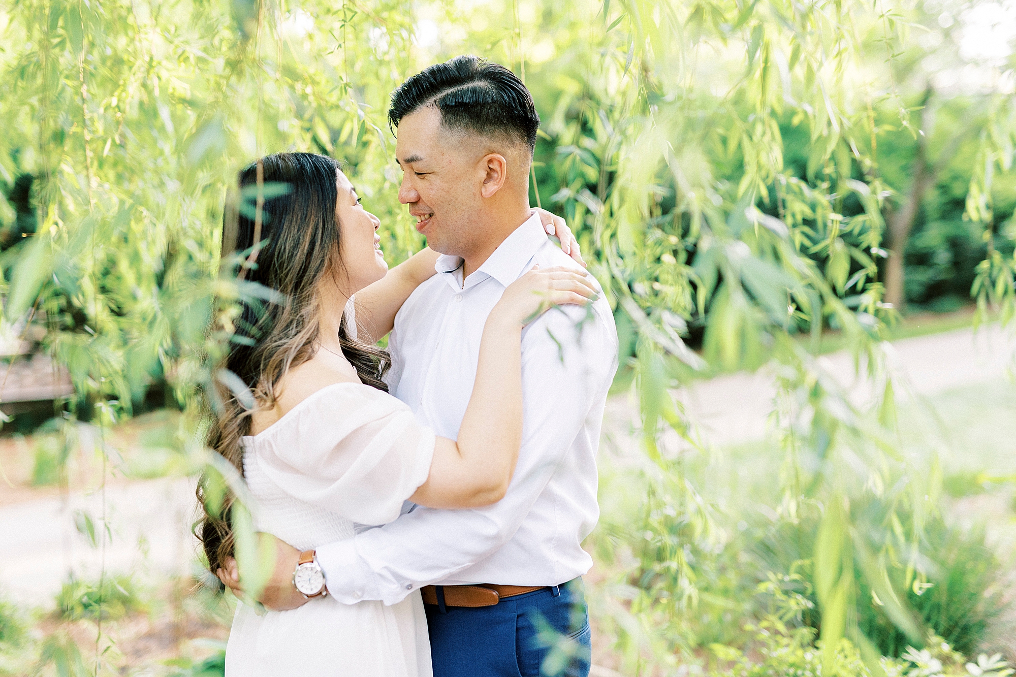 couple hugs between leaves of the weeping willow tree