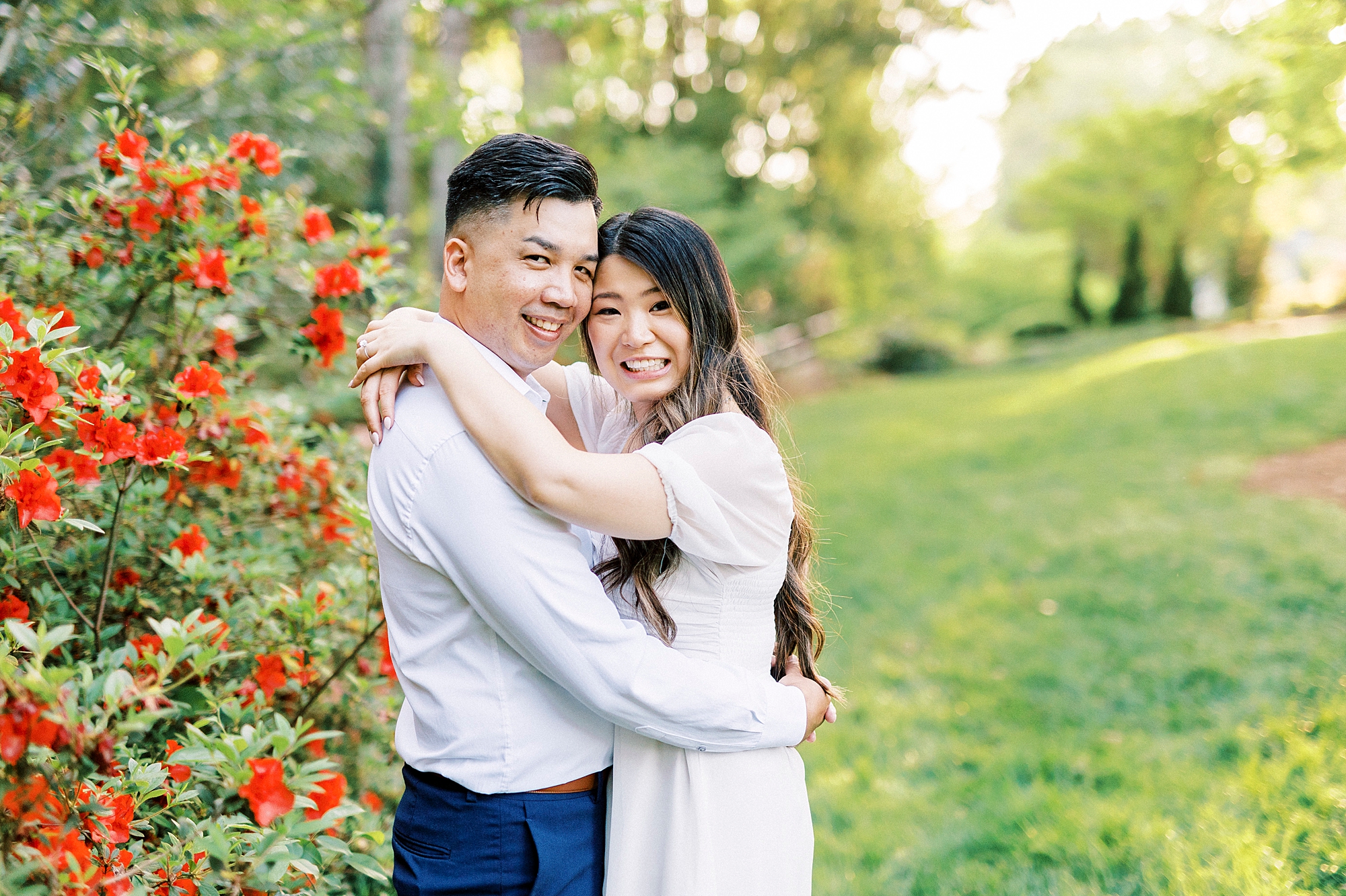 couple hugs by red bush inside Glencairn Garden