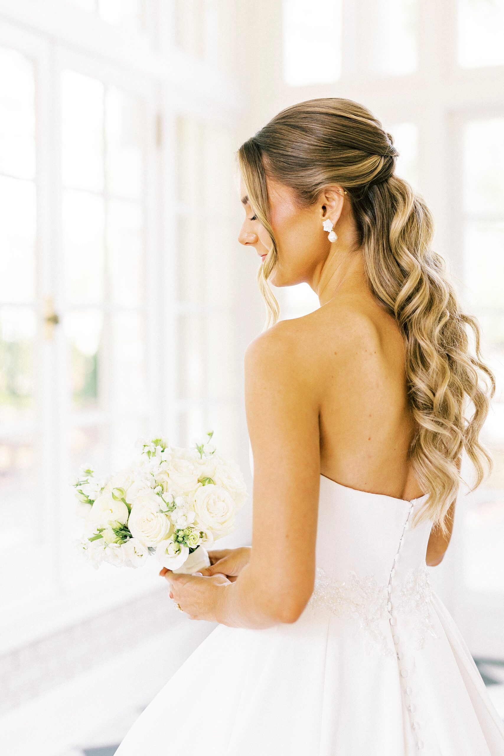 bride holds bouquet of white flowers with curled hair down her back