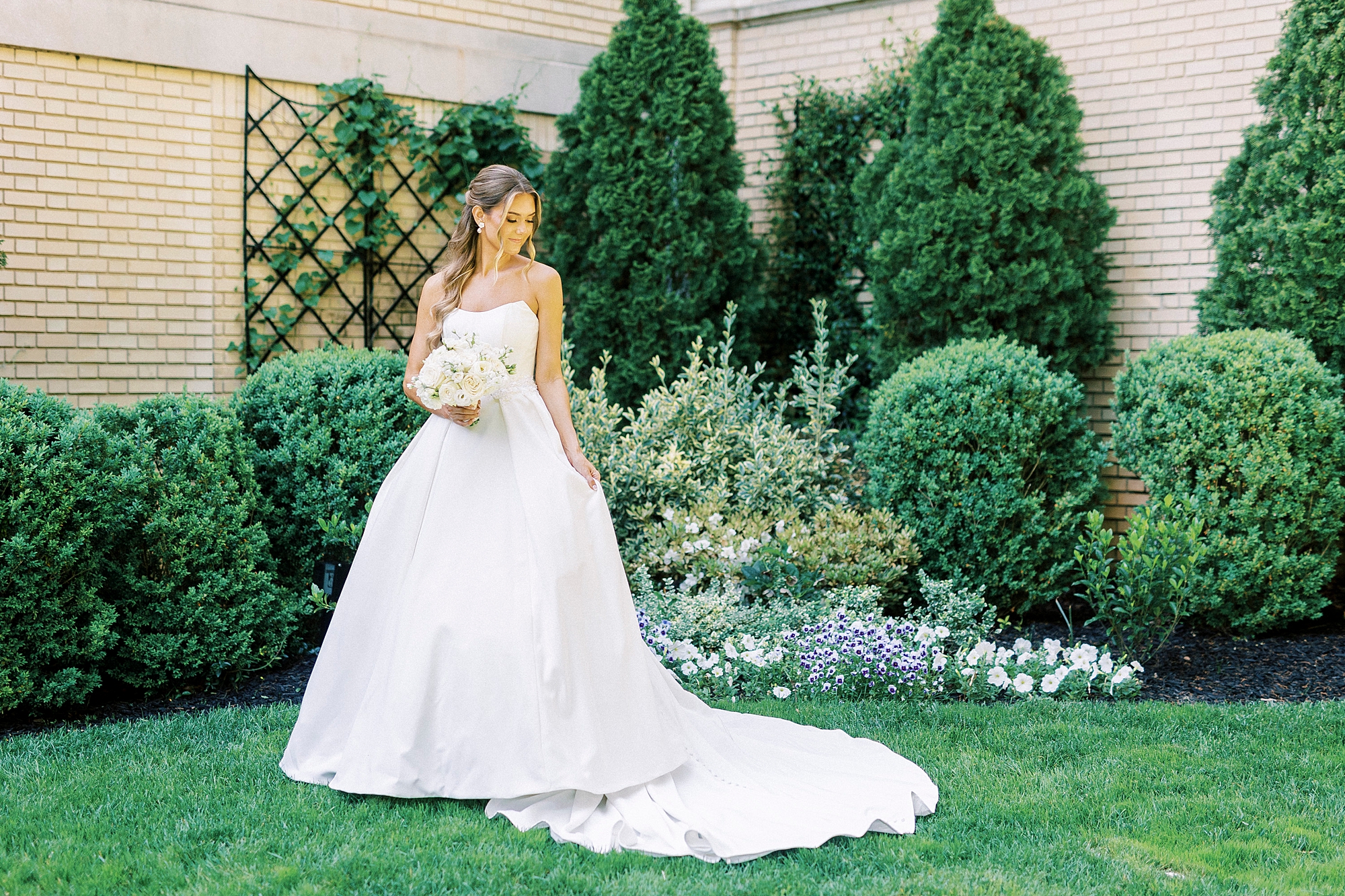 bride holds train of wedding gown looking at grass 