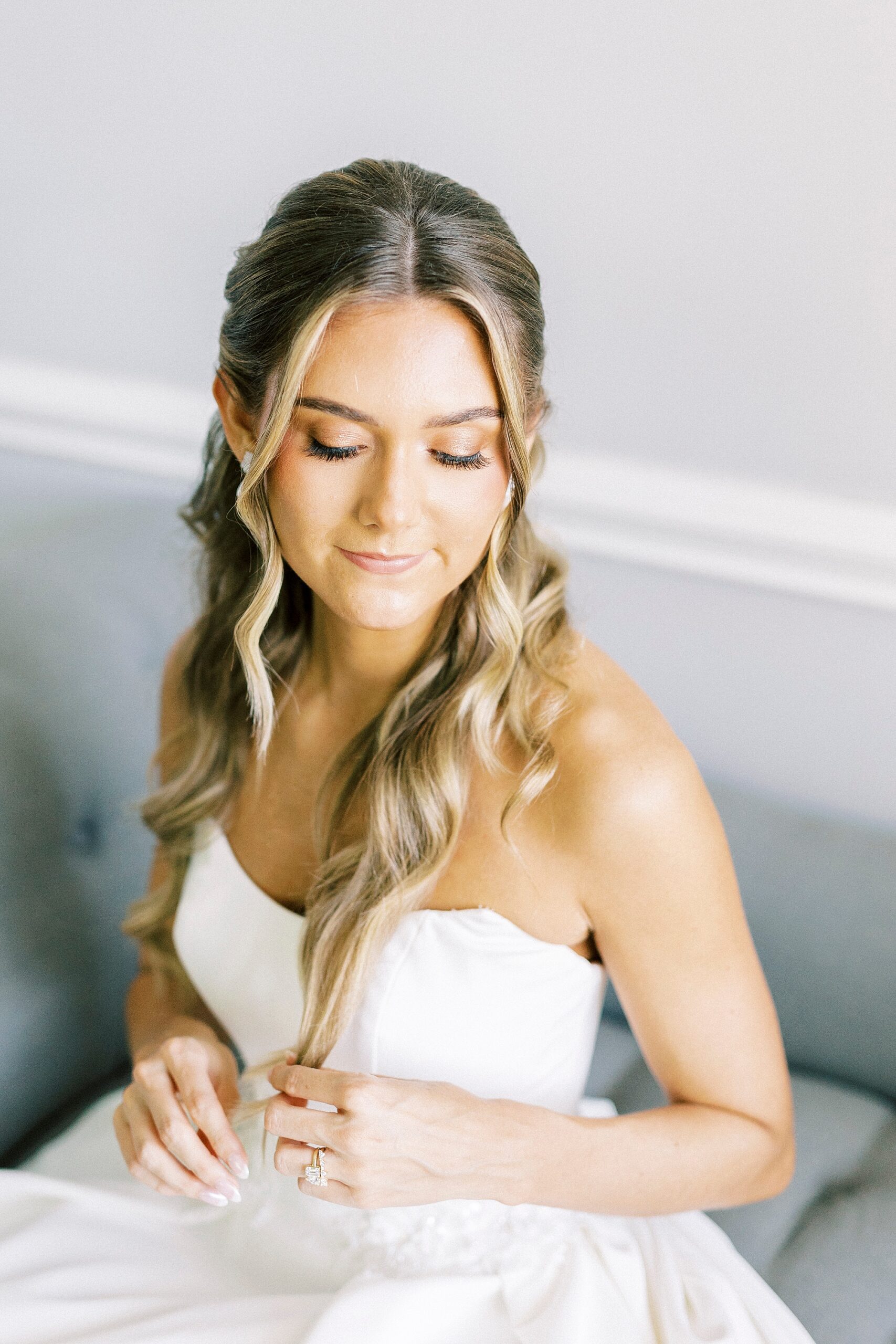 bride sits holding edge of curled hair in front of her chest 