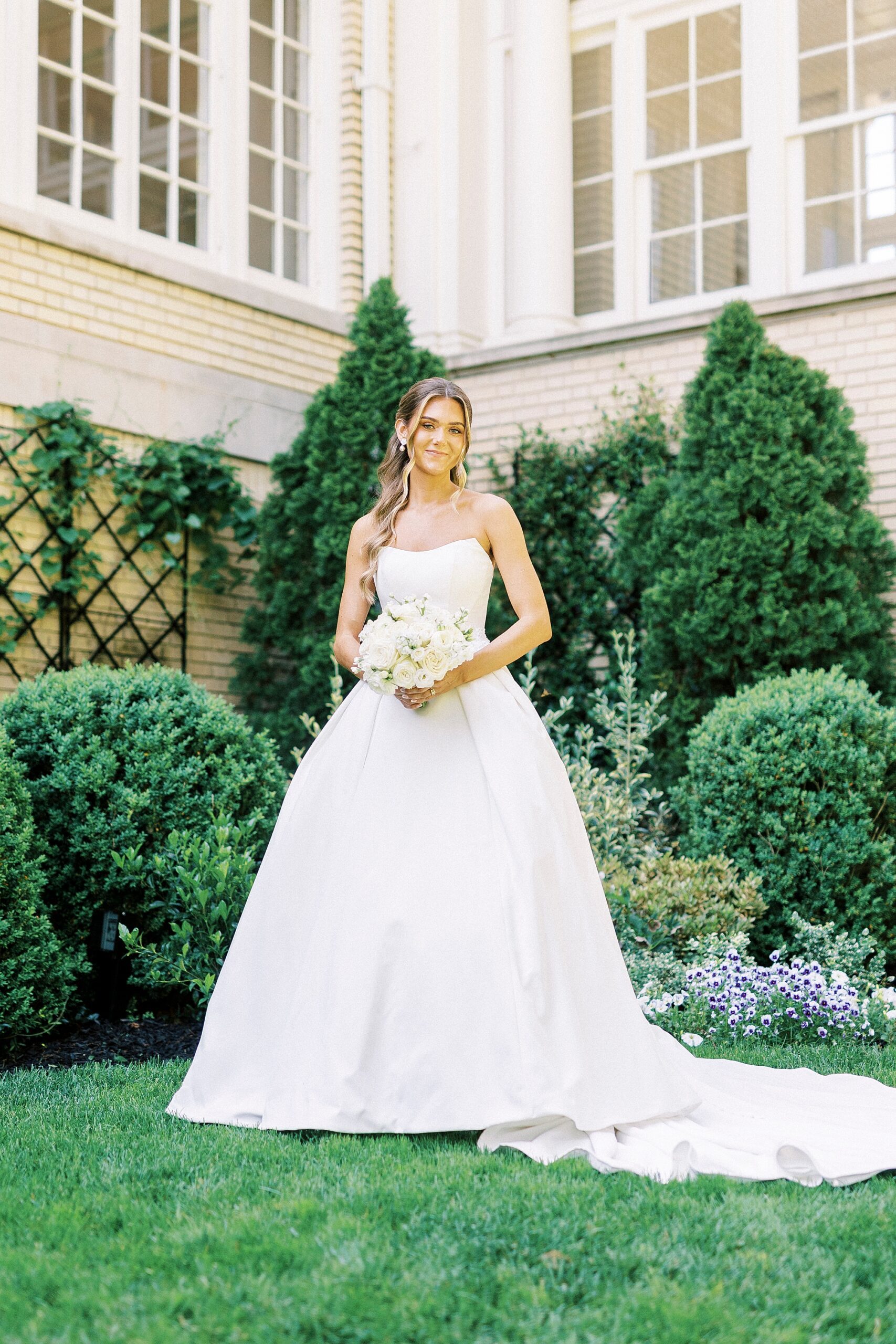 bride holds bouquet of ivory flowers in front of greenery in garden