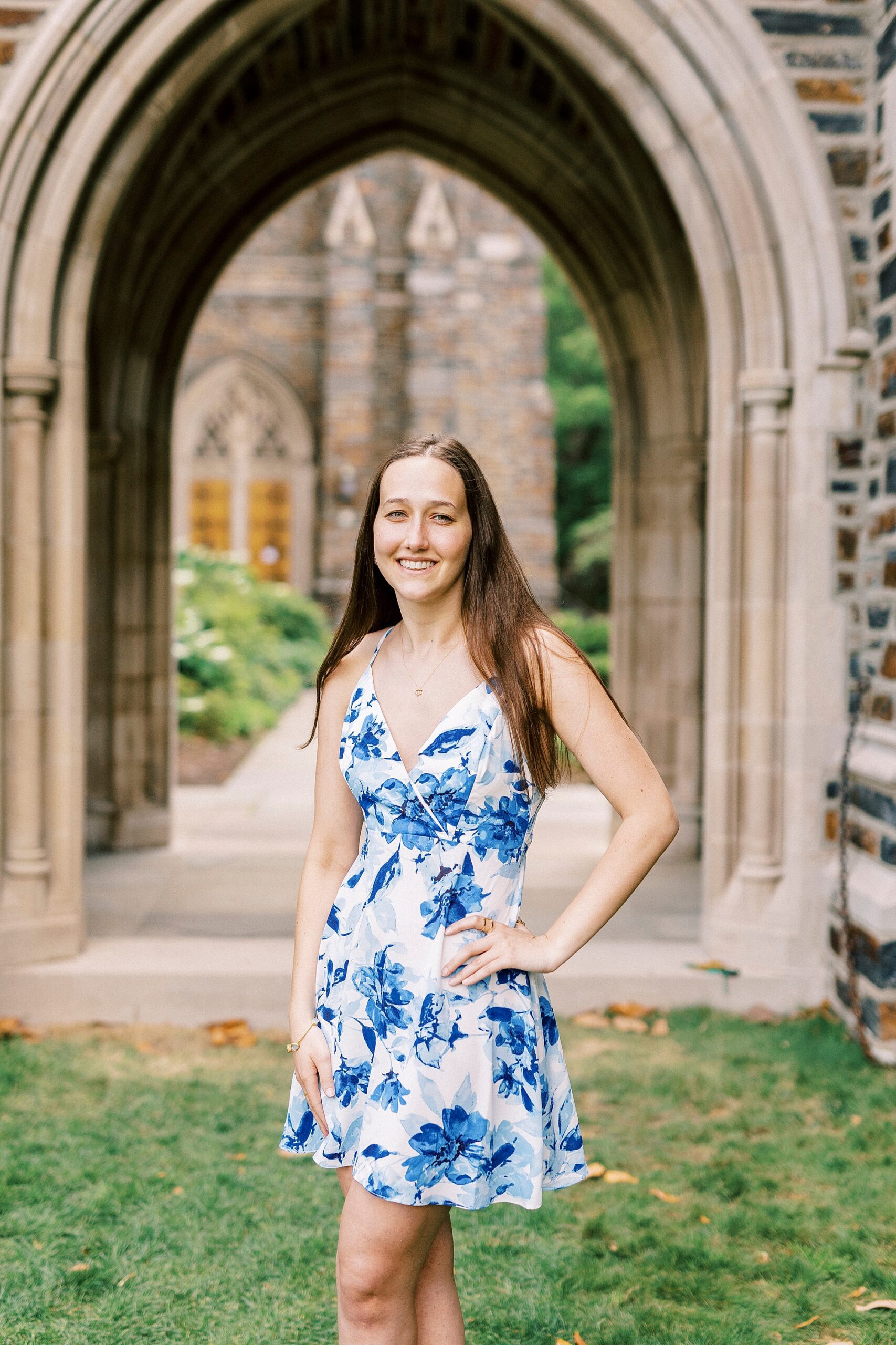 graduate stands in front of brick archway at Duke University chapel with hand on her hip
