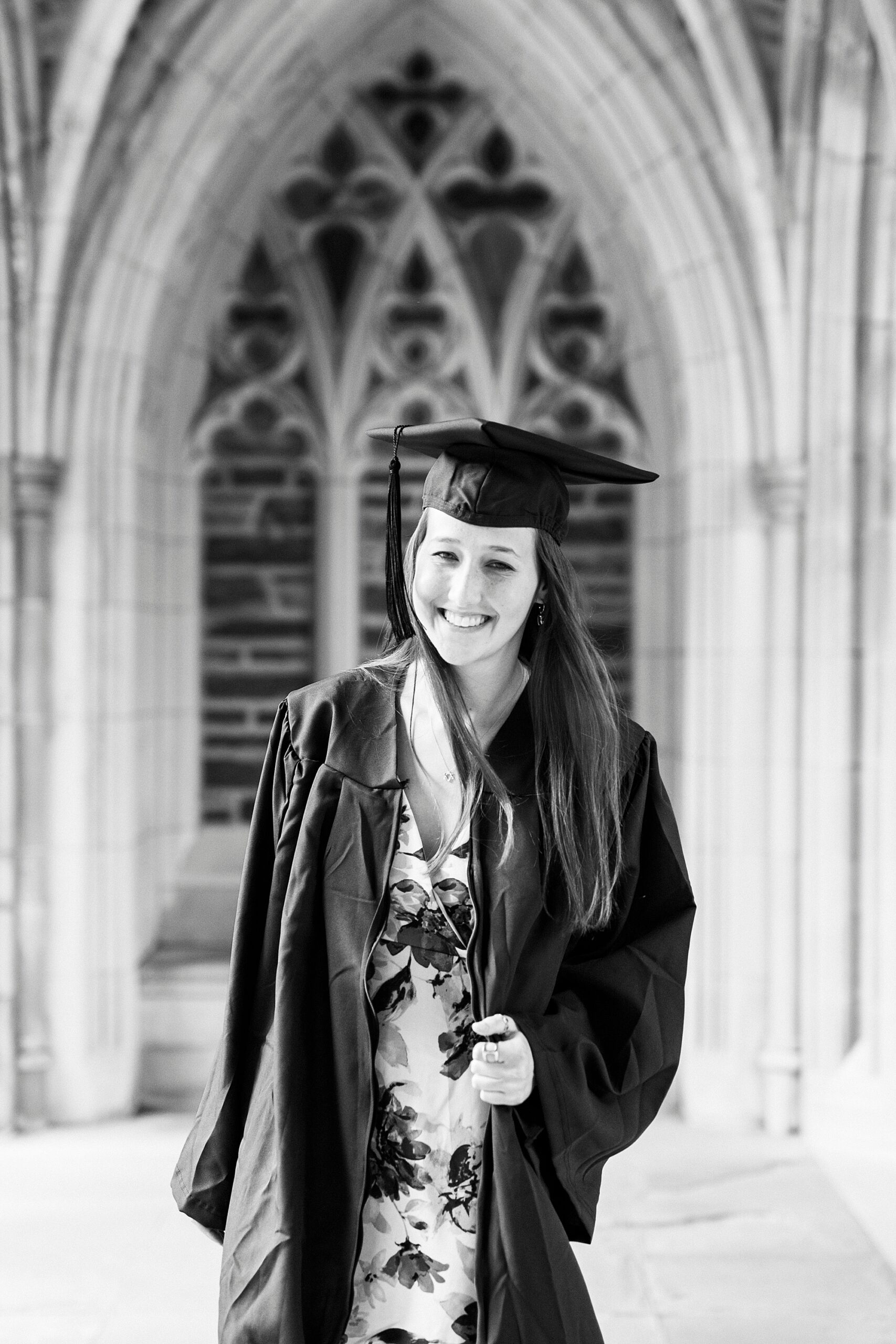 senior leans forward wearing cap and gown in archways of Duke University chapel