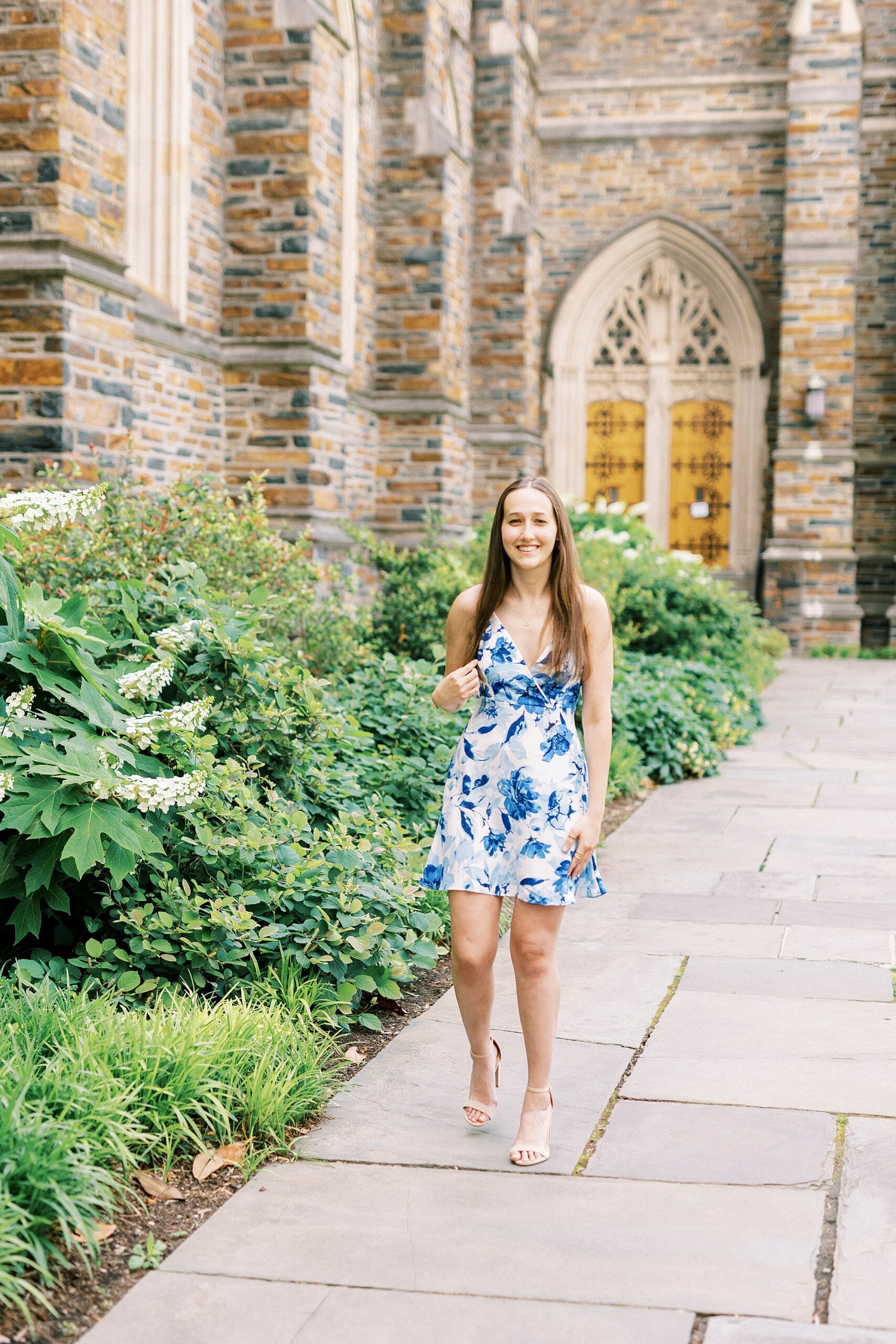 girl walks outside chapel in blue and white dress for Duke University senior portraits