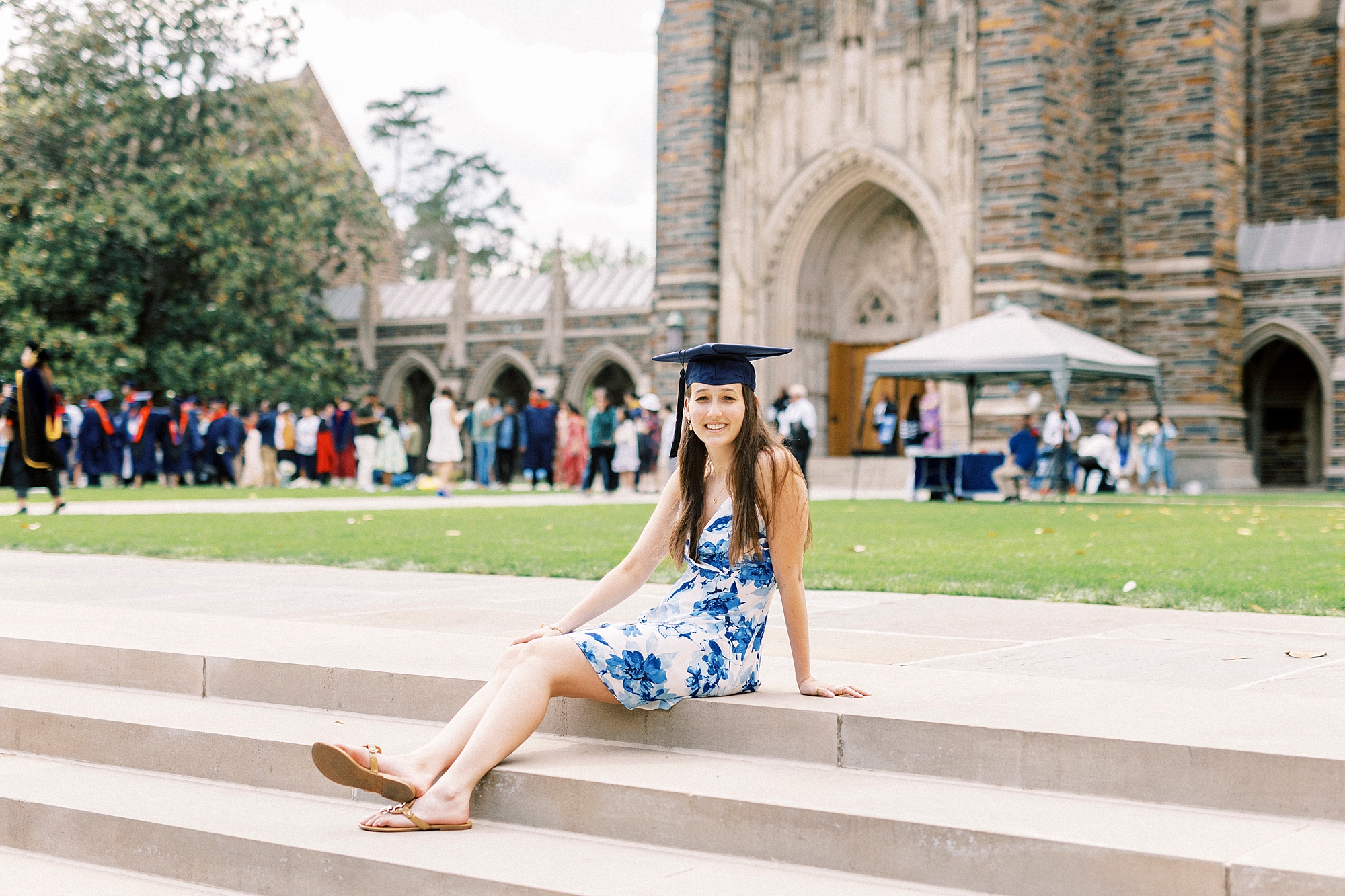 senior sits on steps in front of chapel wearing cap with dress 