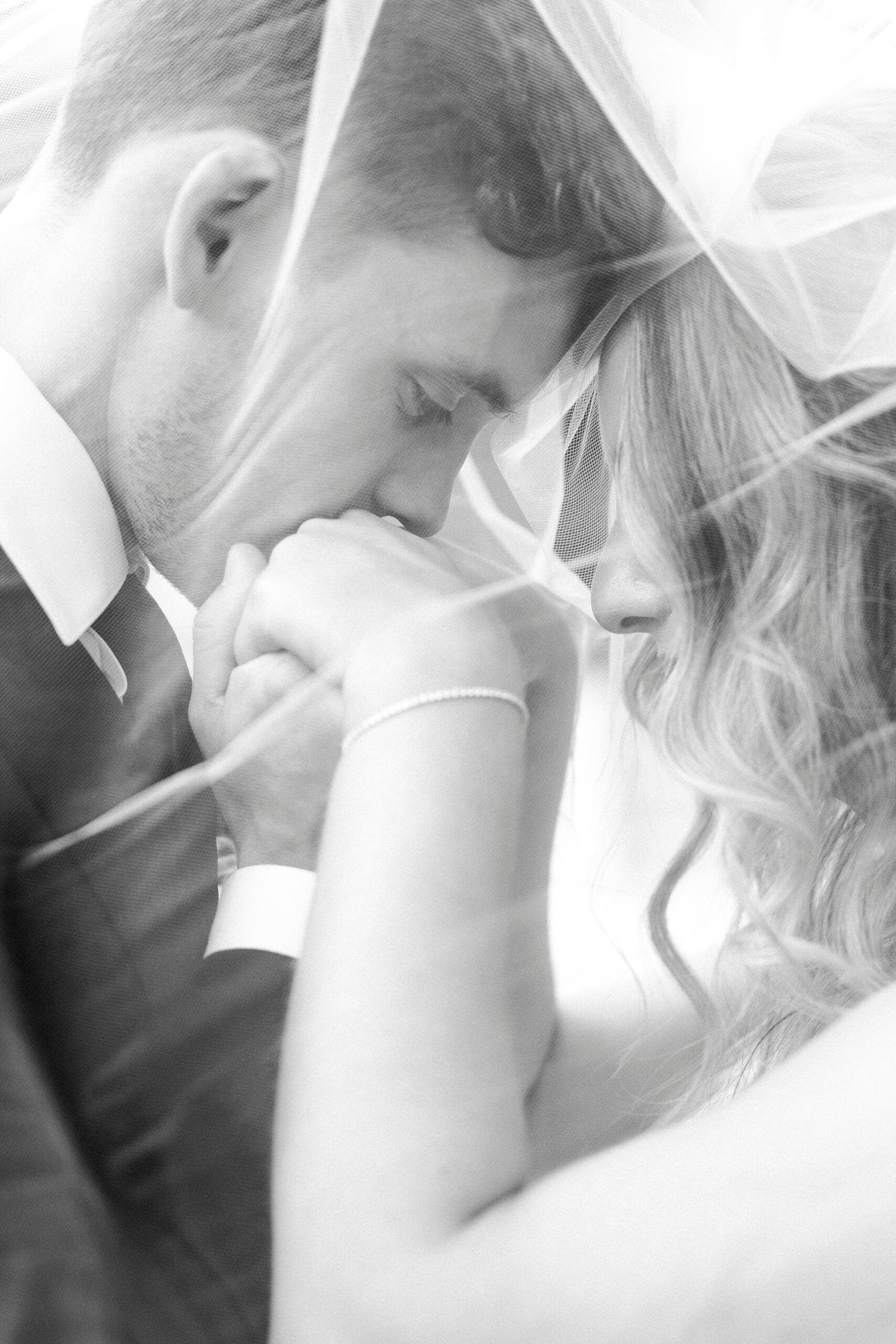 groom holds bride's hand kissing them under veil 