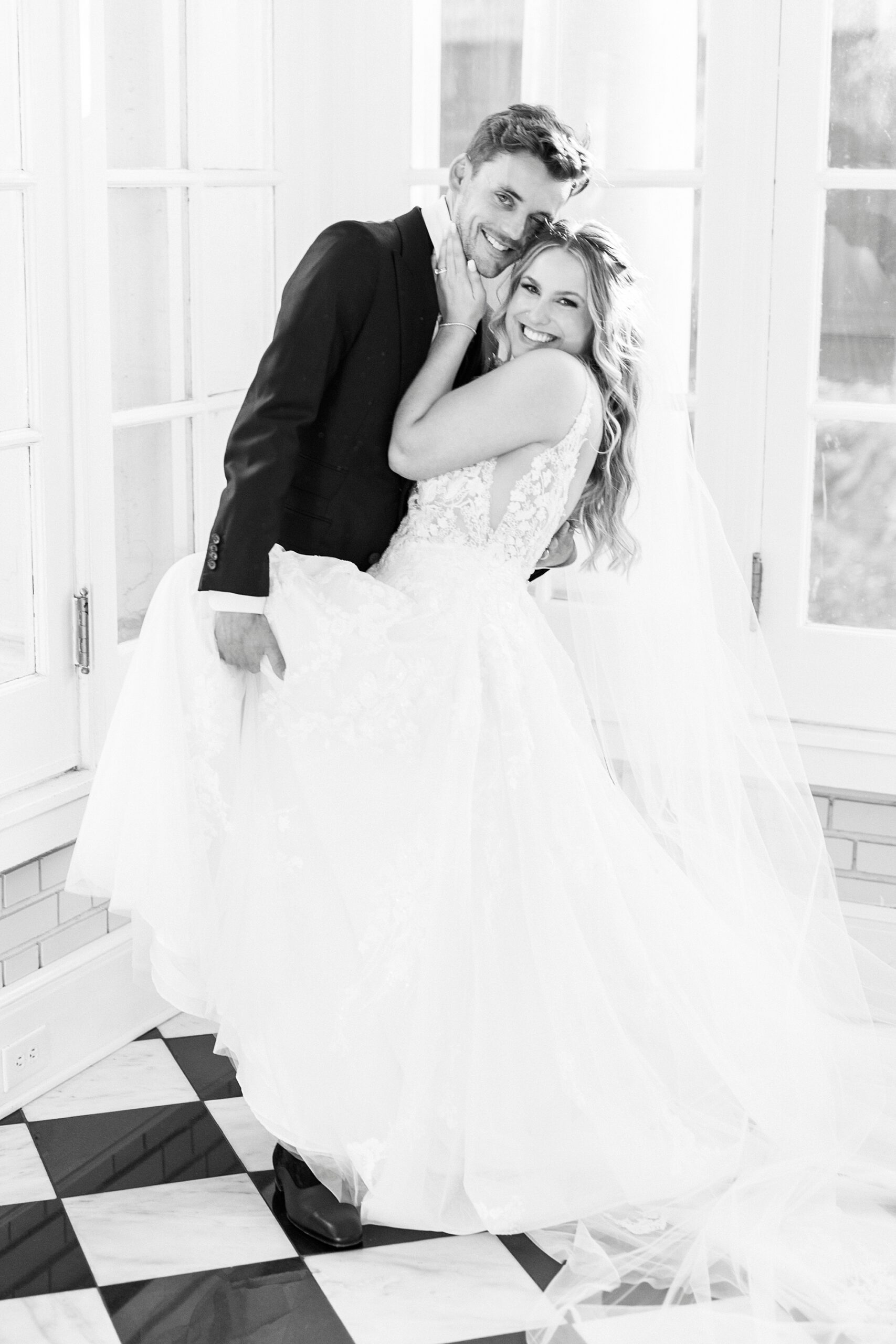 groom hugs bride holding her leg up by them in sunroom of Separk Mansion