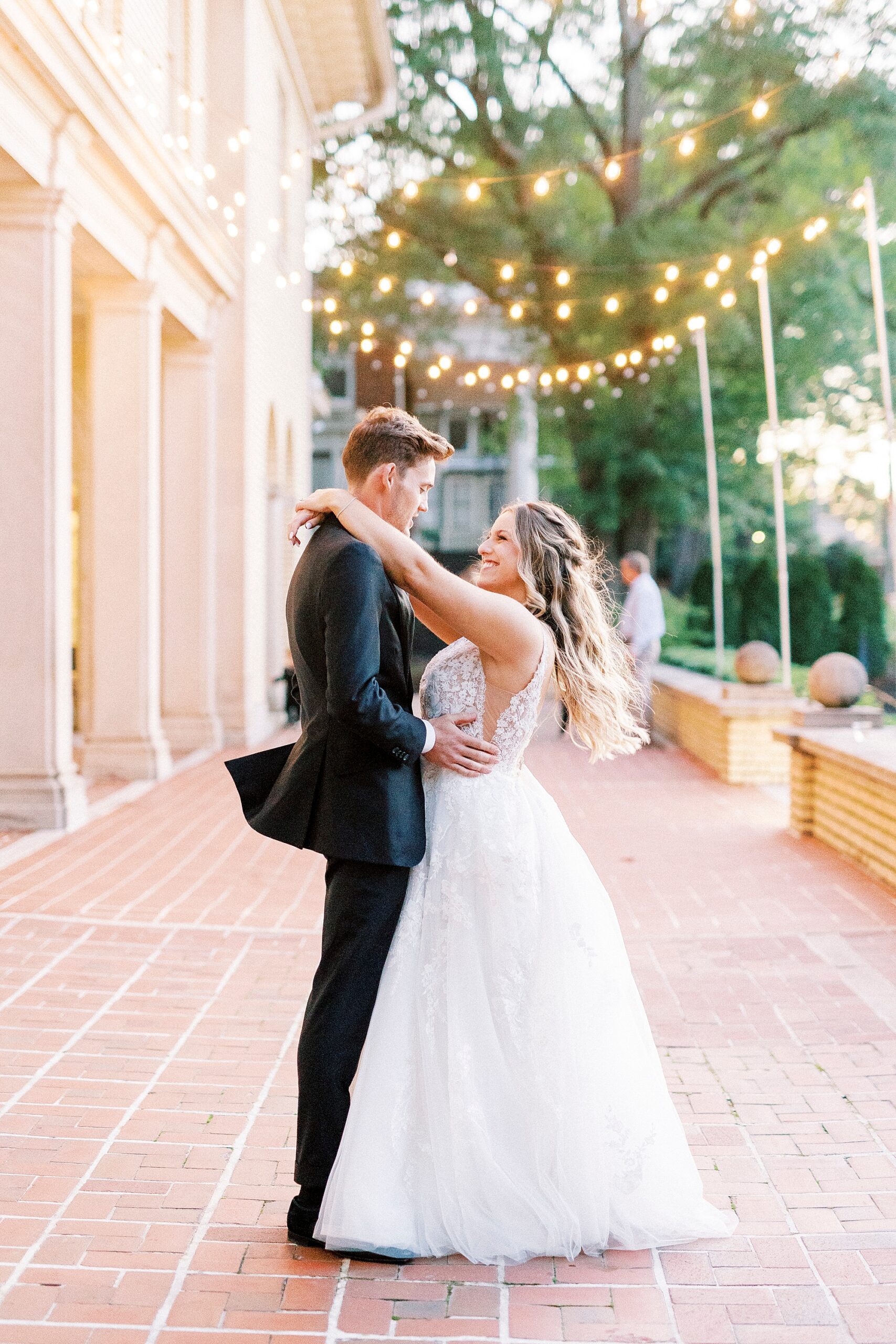 bride and groom hug on brick patio with bistro lights hanging above them at Separk Mansion