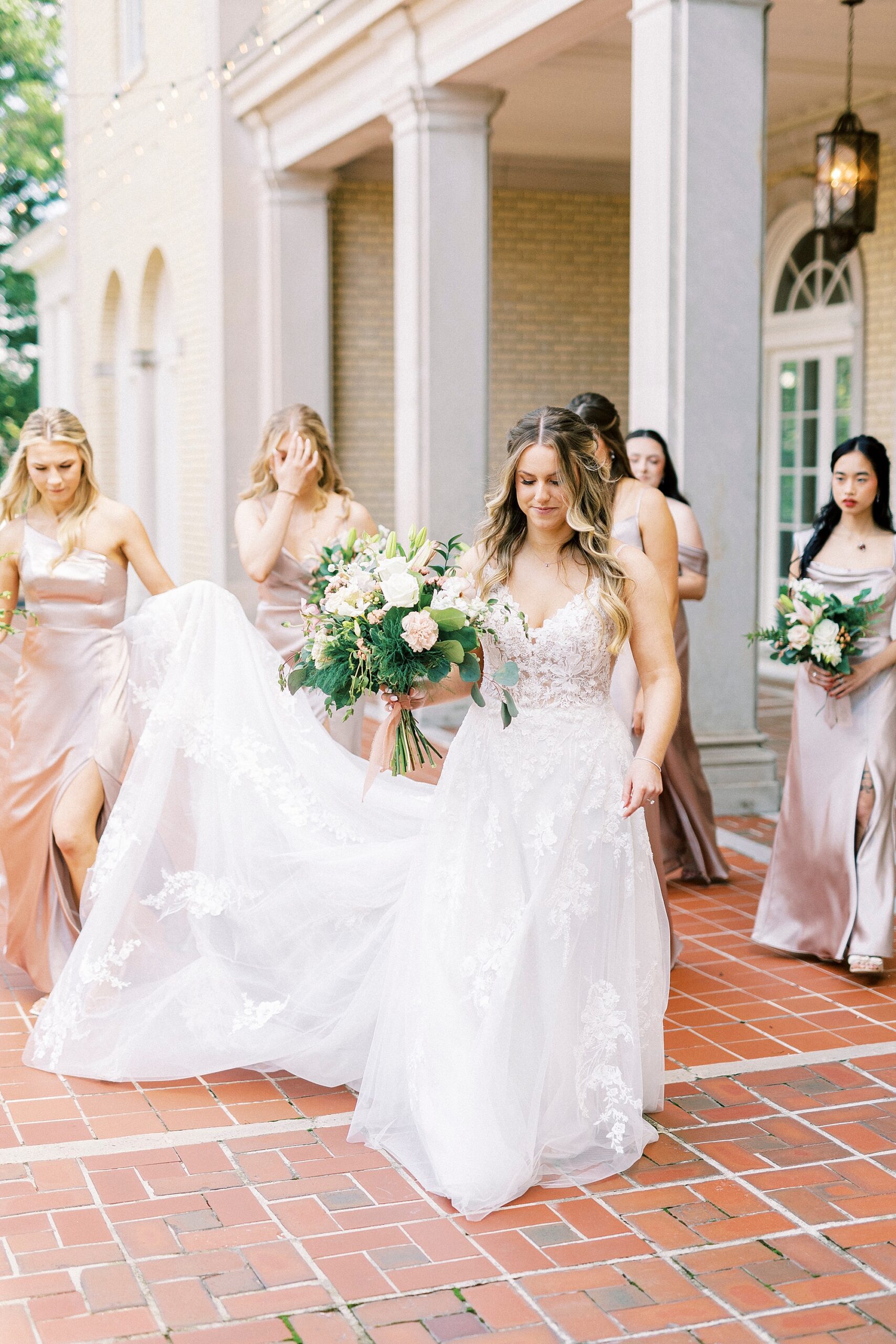 bride walks on patio at Separk Mansion with bridesmaids in pink satin gowns 