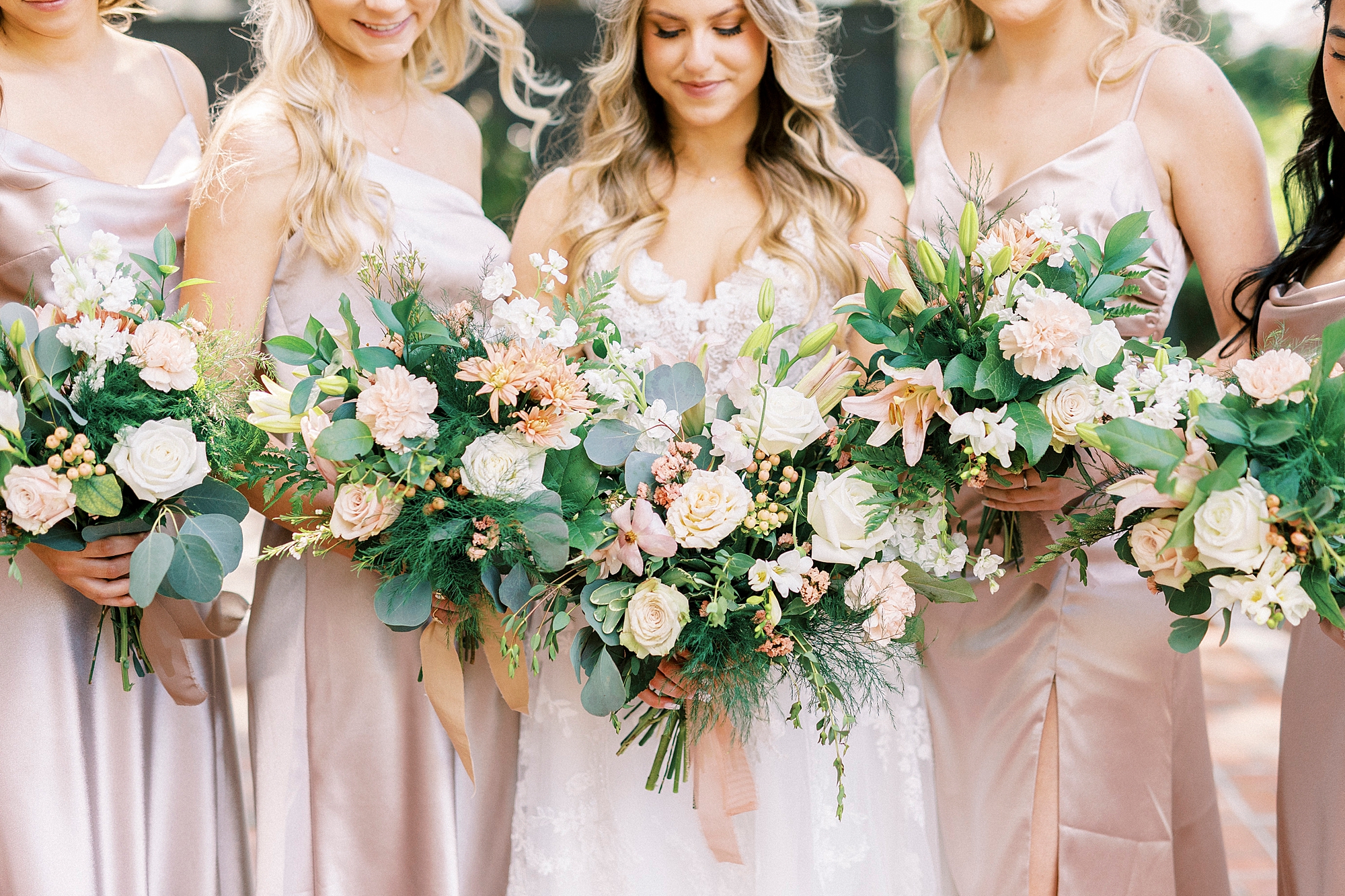 bride stands with bridesmaids in pink satin dresses with white and pink flowers 