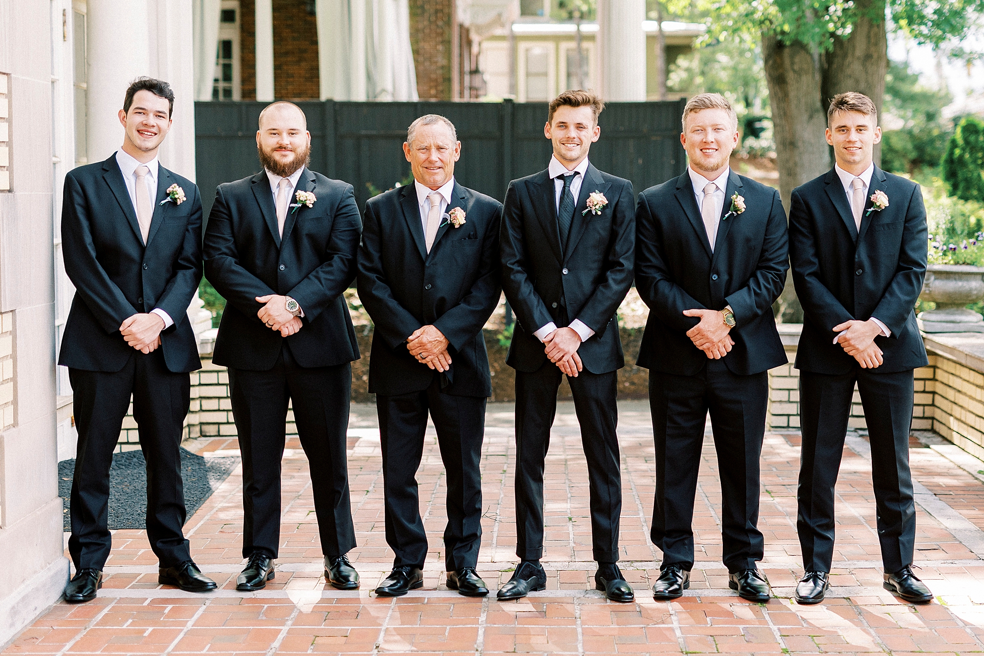groom stands with groomsmen in black suits outside Separk Mansion