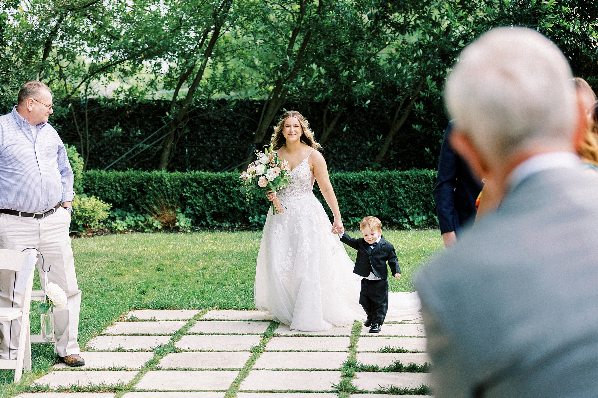 bride walks down aisle with toddler son in gardens of Separk Mansion