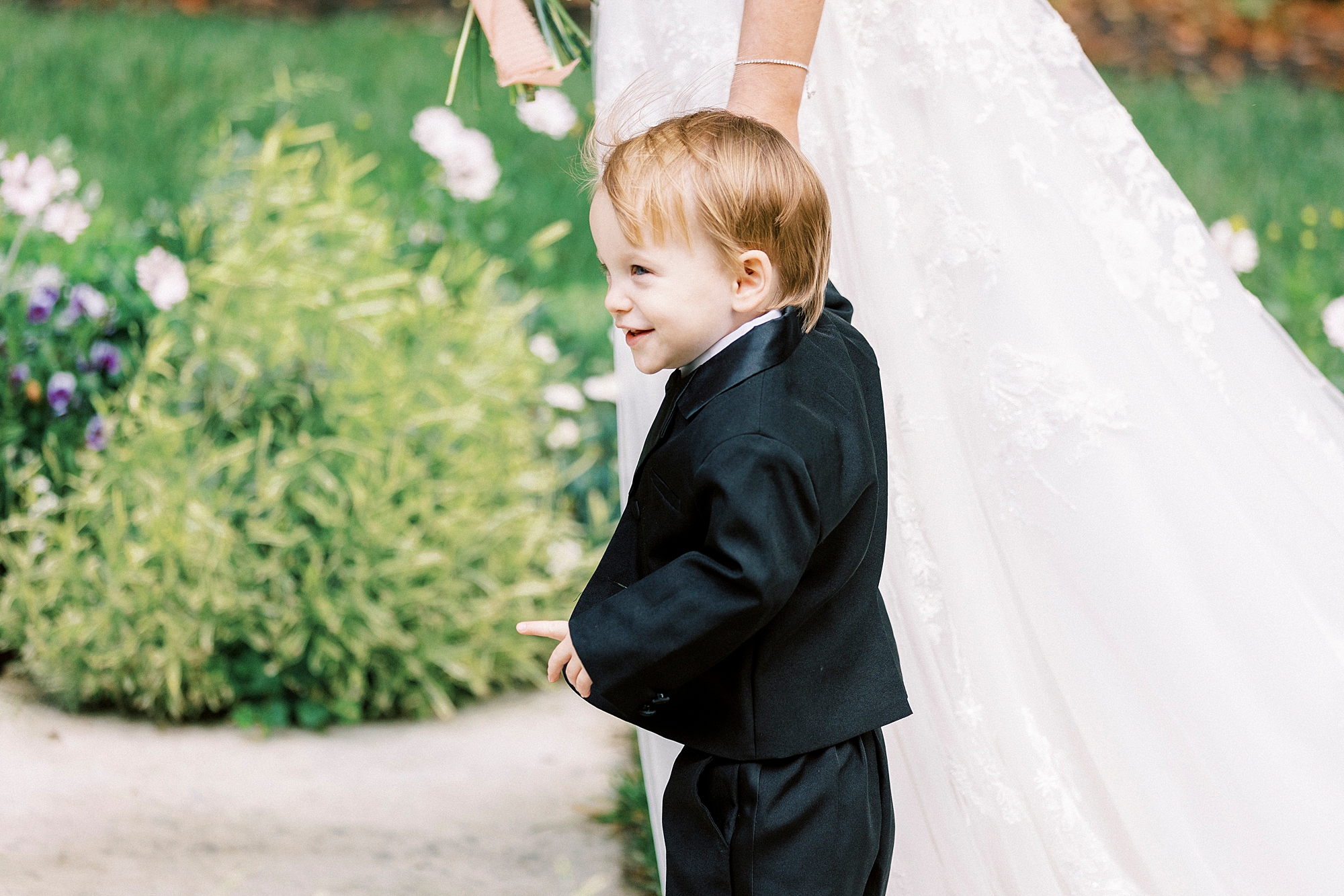 young toddler smiles holding mom's hand during ceremony in garden 