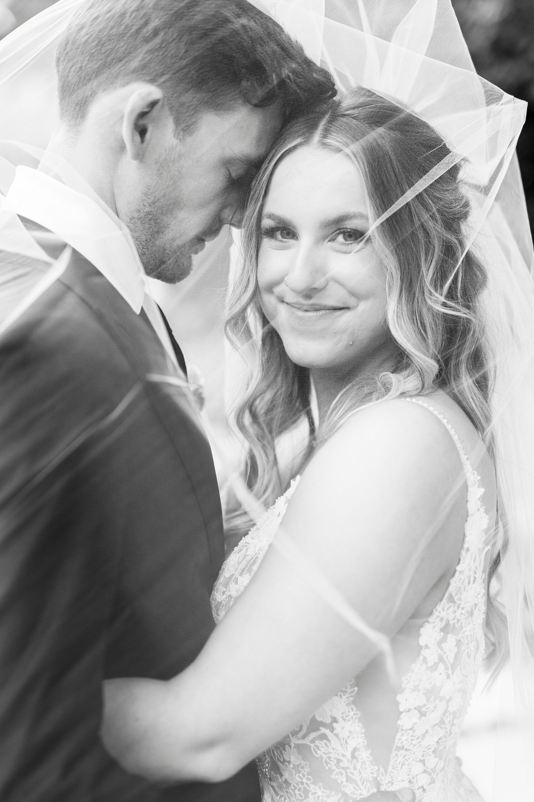 newlyweds hug under veil smiling in Charlotte NC