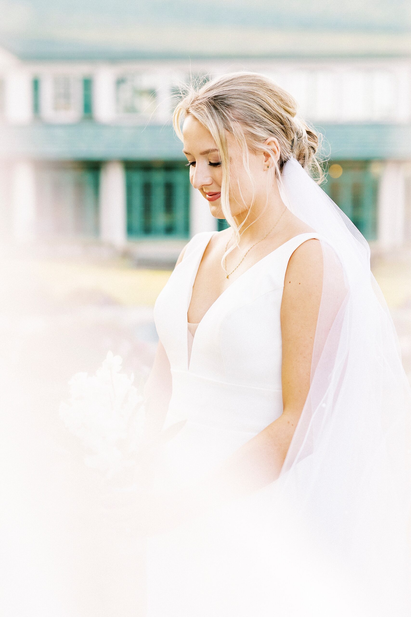 bride looks down at bouquet with veil floating around her