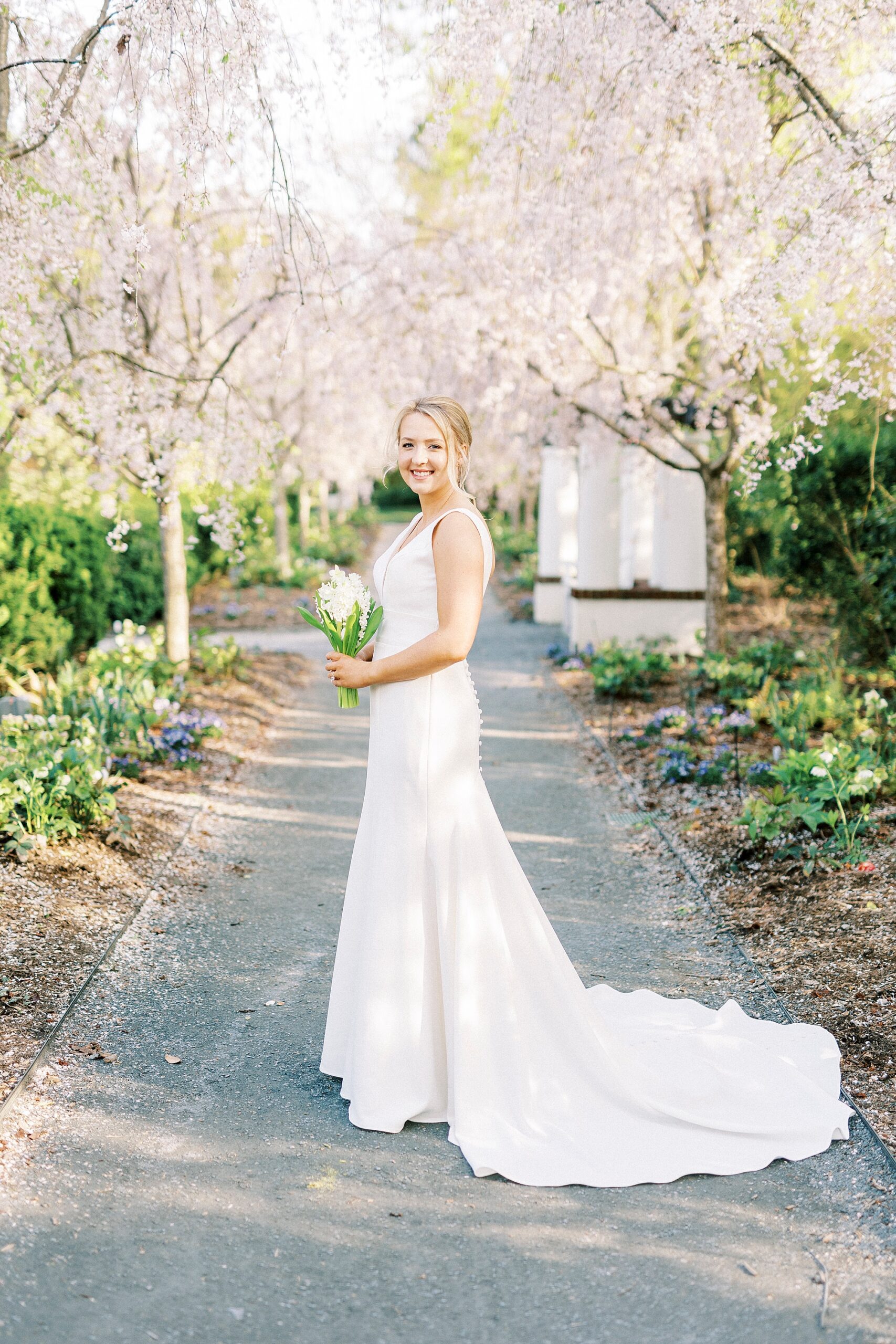 bride holds bouquet of white flowers under pink trees at Reynolda Gardens