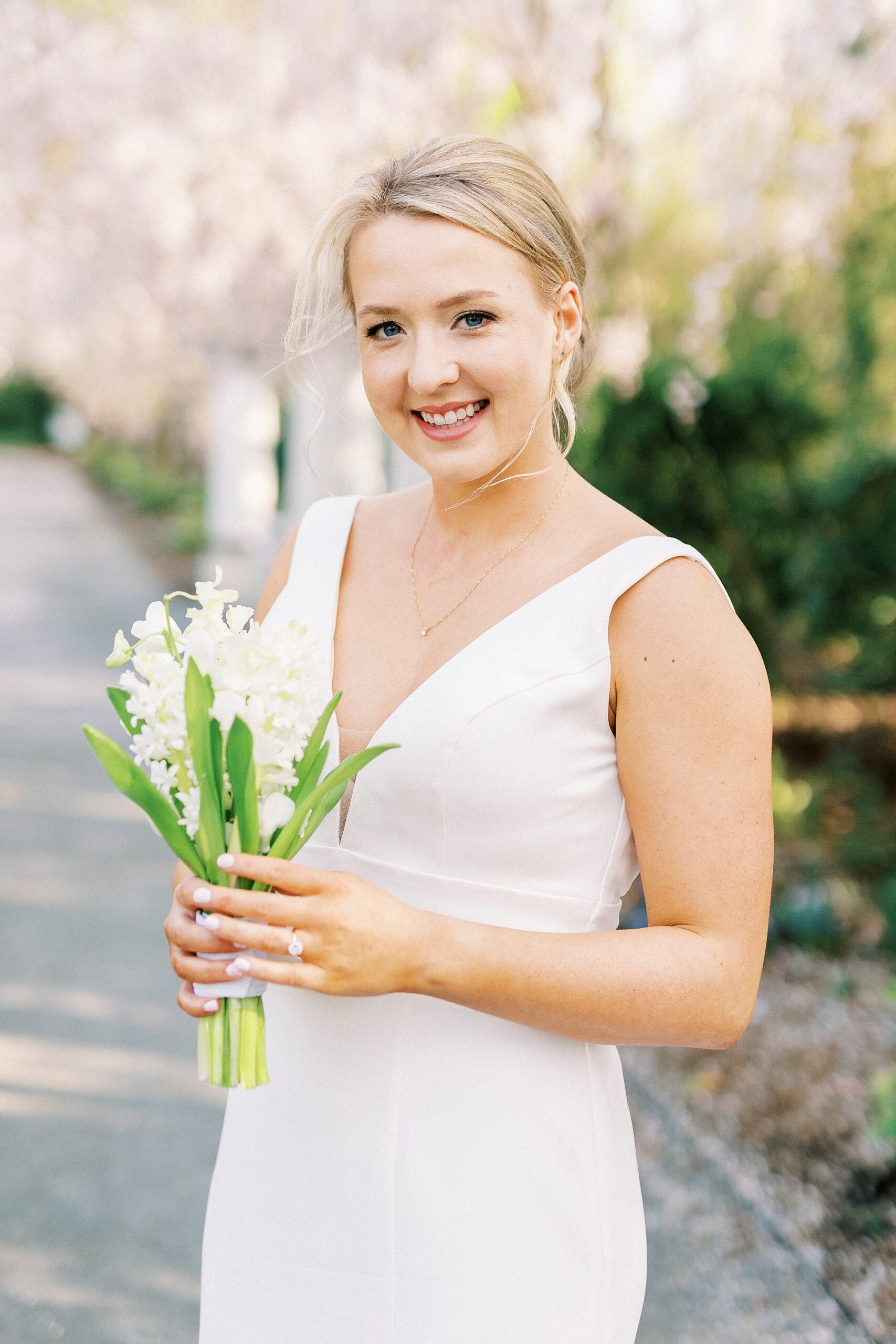 bride grins holding bouquet of white flowers at Reynolda Gardens