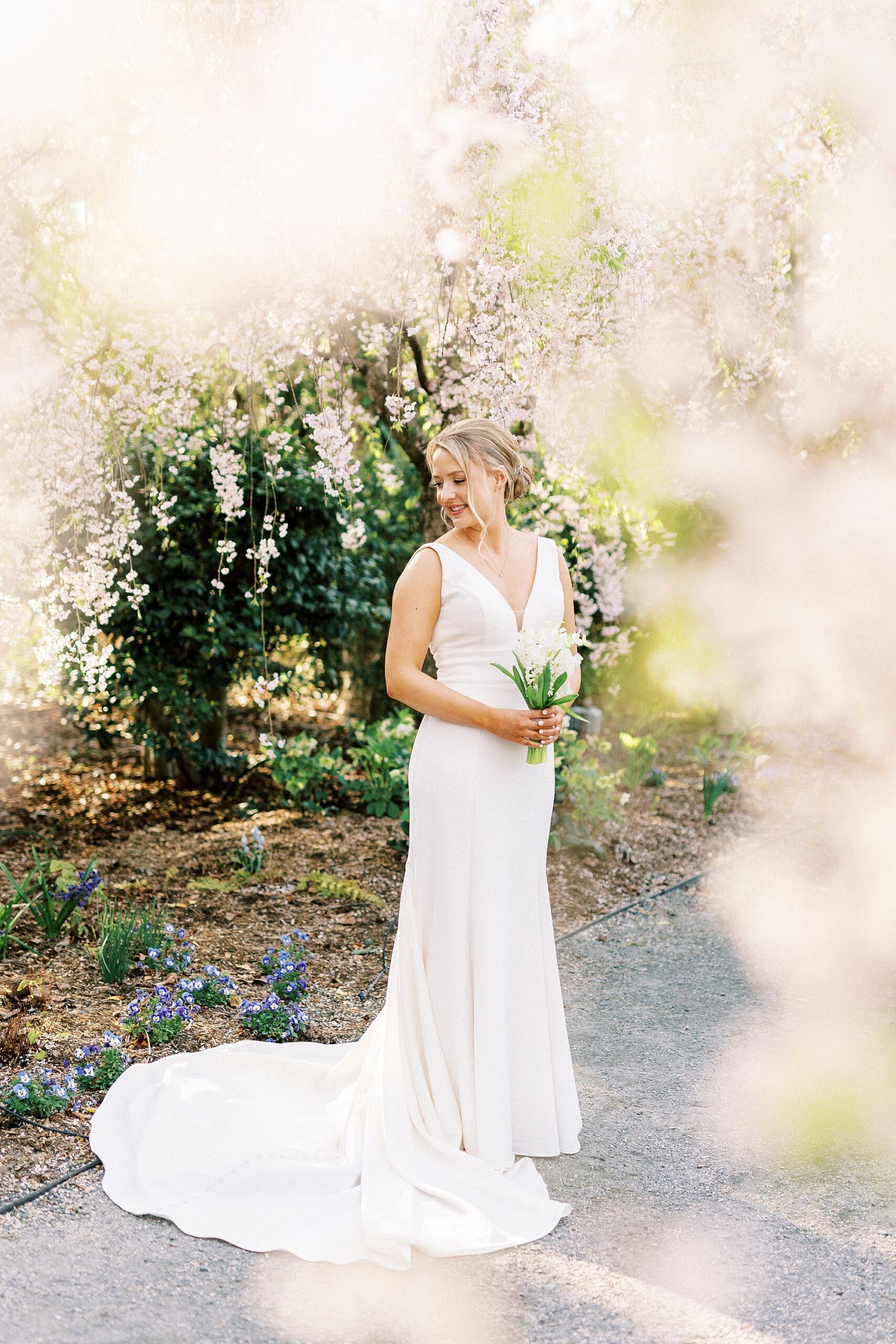 bride grins over shoulder in wedding gown with pink blossoms in foreground