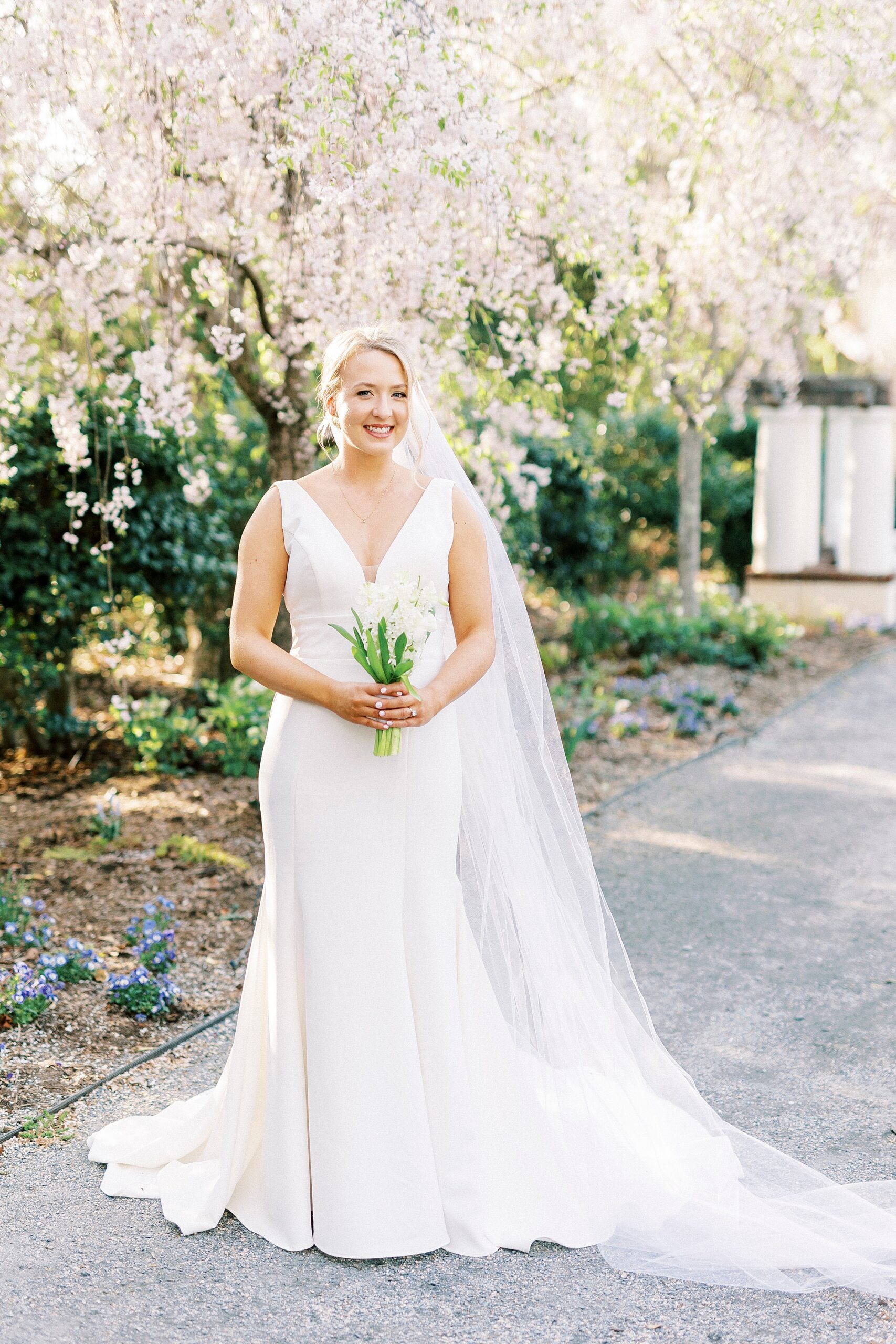 bride holds bouquet of white hyacinths on path with veil around her shoulders at Reynolda Gardens