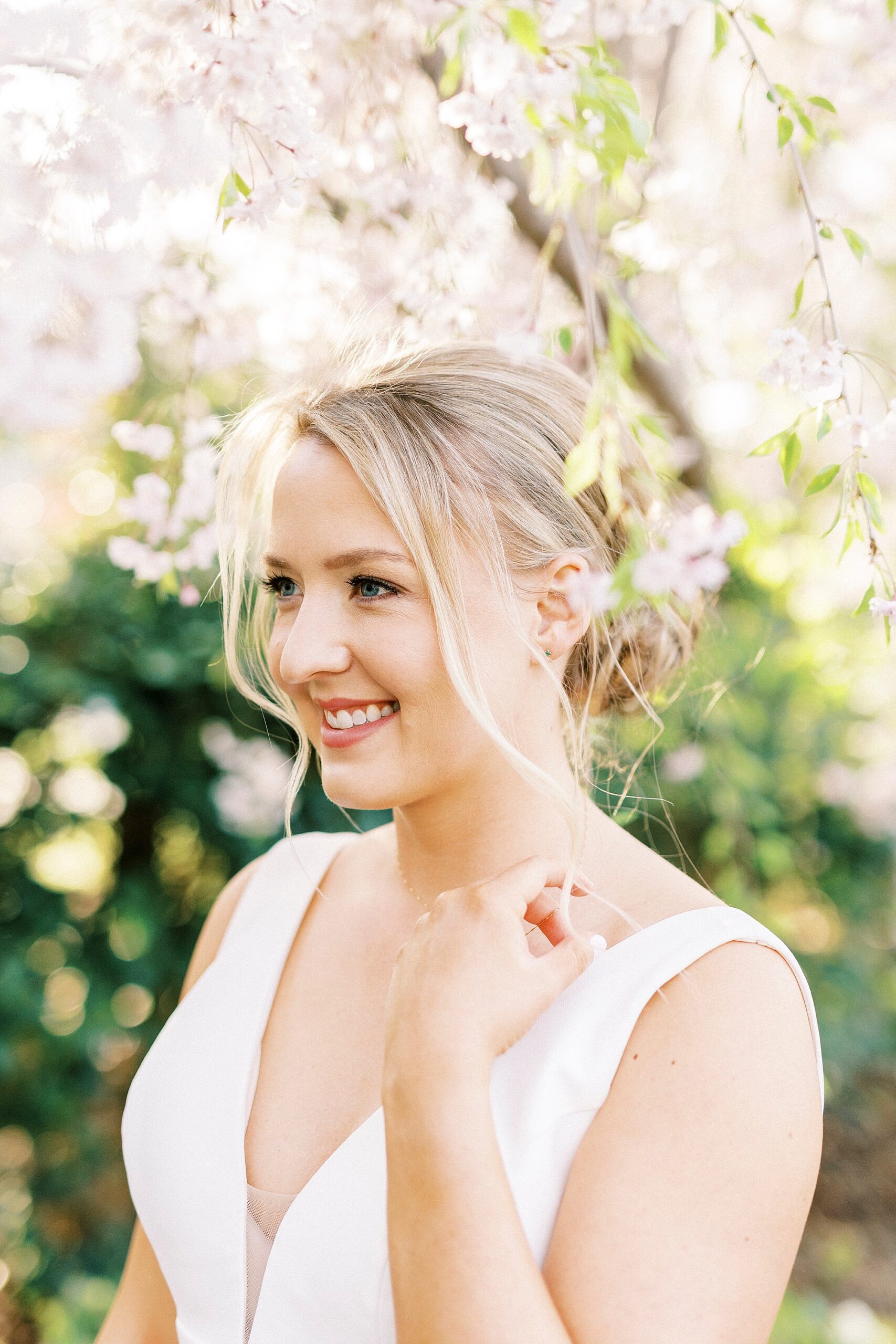 bride holds strap of wedding gown under pink blossoms at Reynolda Gardens