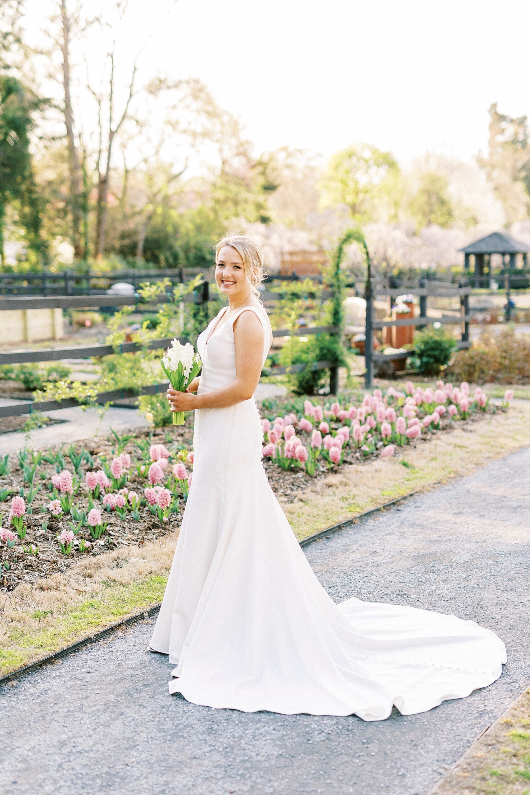 bride grins looking over shoulder in front of pink flowers at Reynolda Gardens