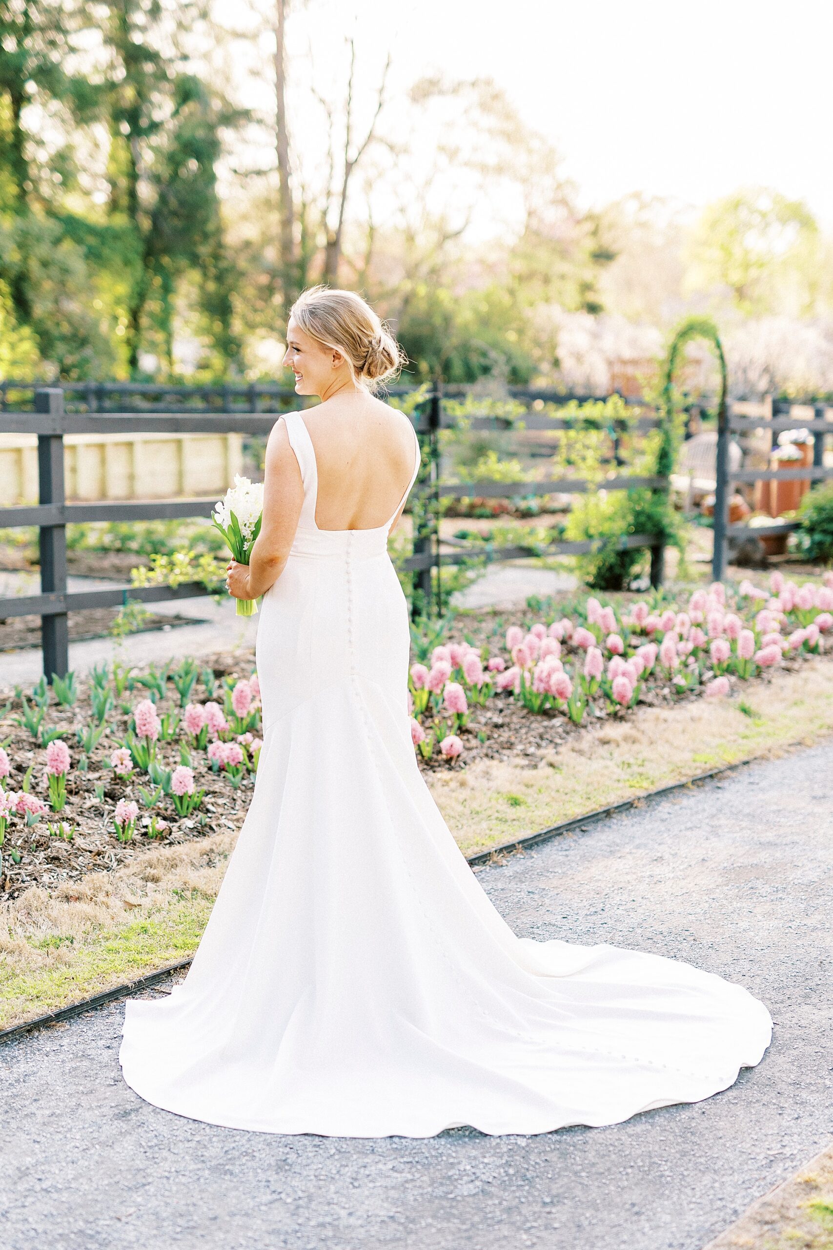 bride looks at pink flowers showing off back of wedding gown