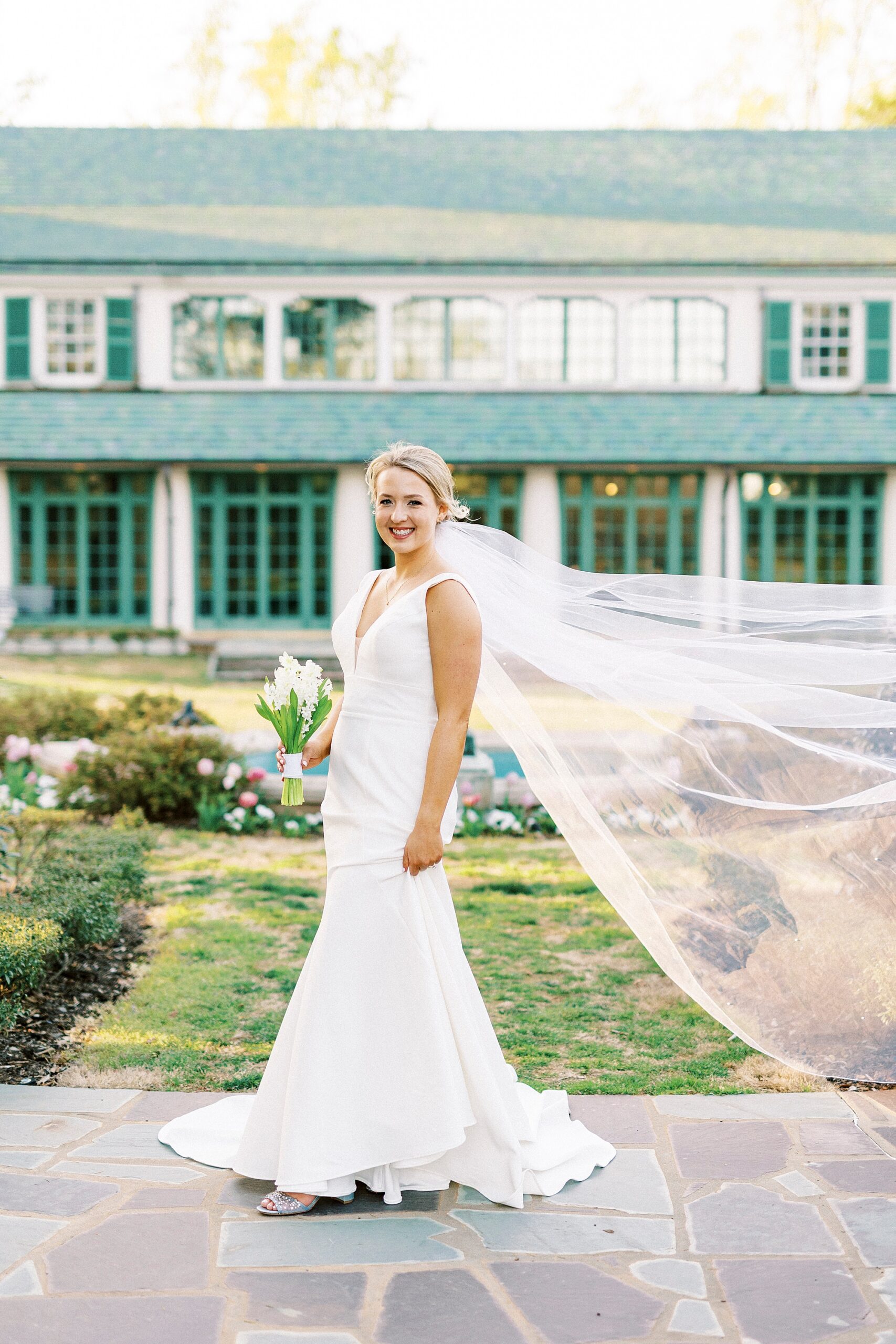 bride smiles with veil floating behind her inside Reynolda Gardens