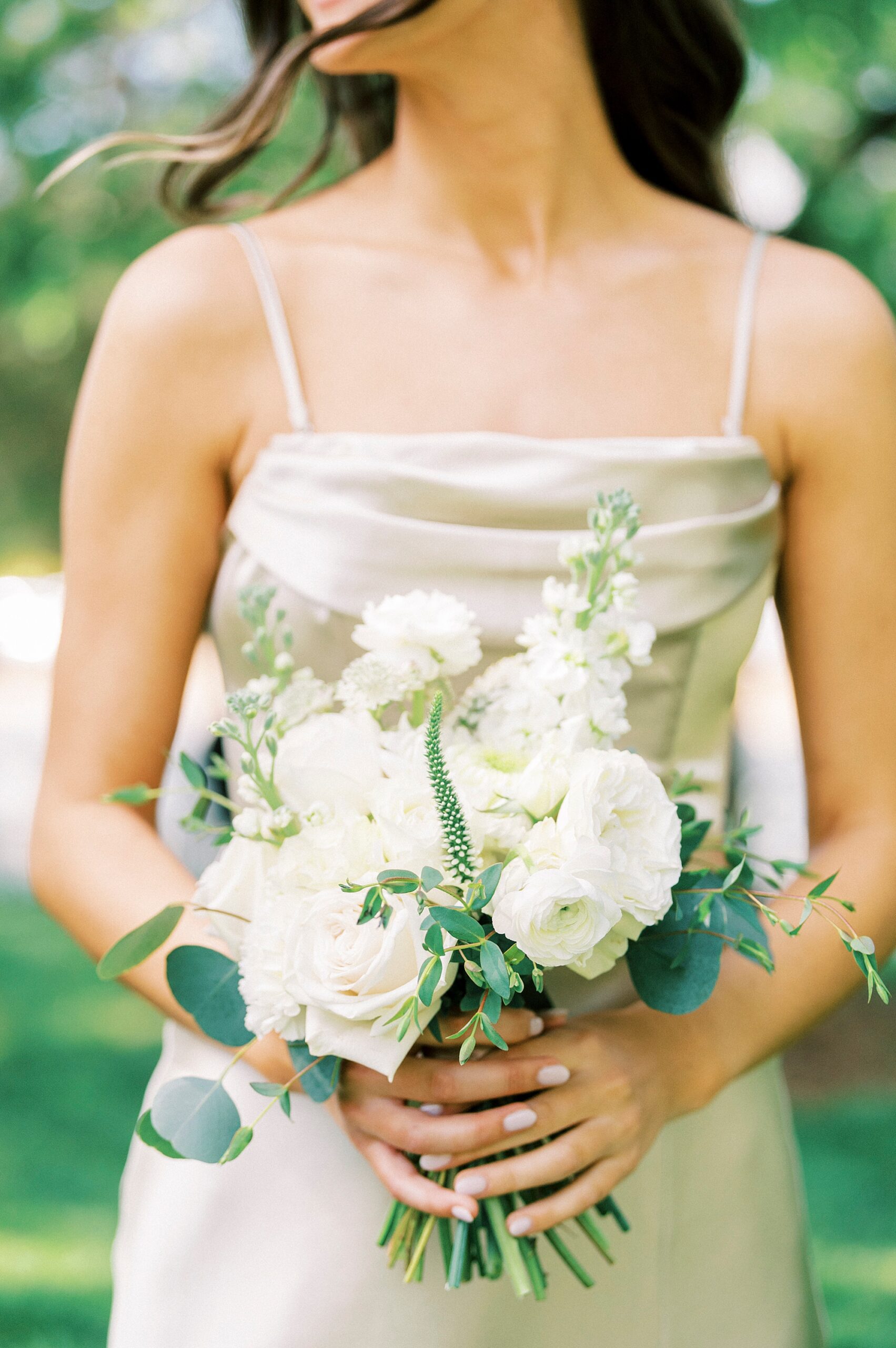 bridesmaid in satin gown holds small bouquet of white flowers
