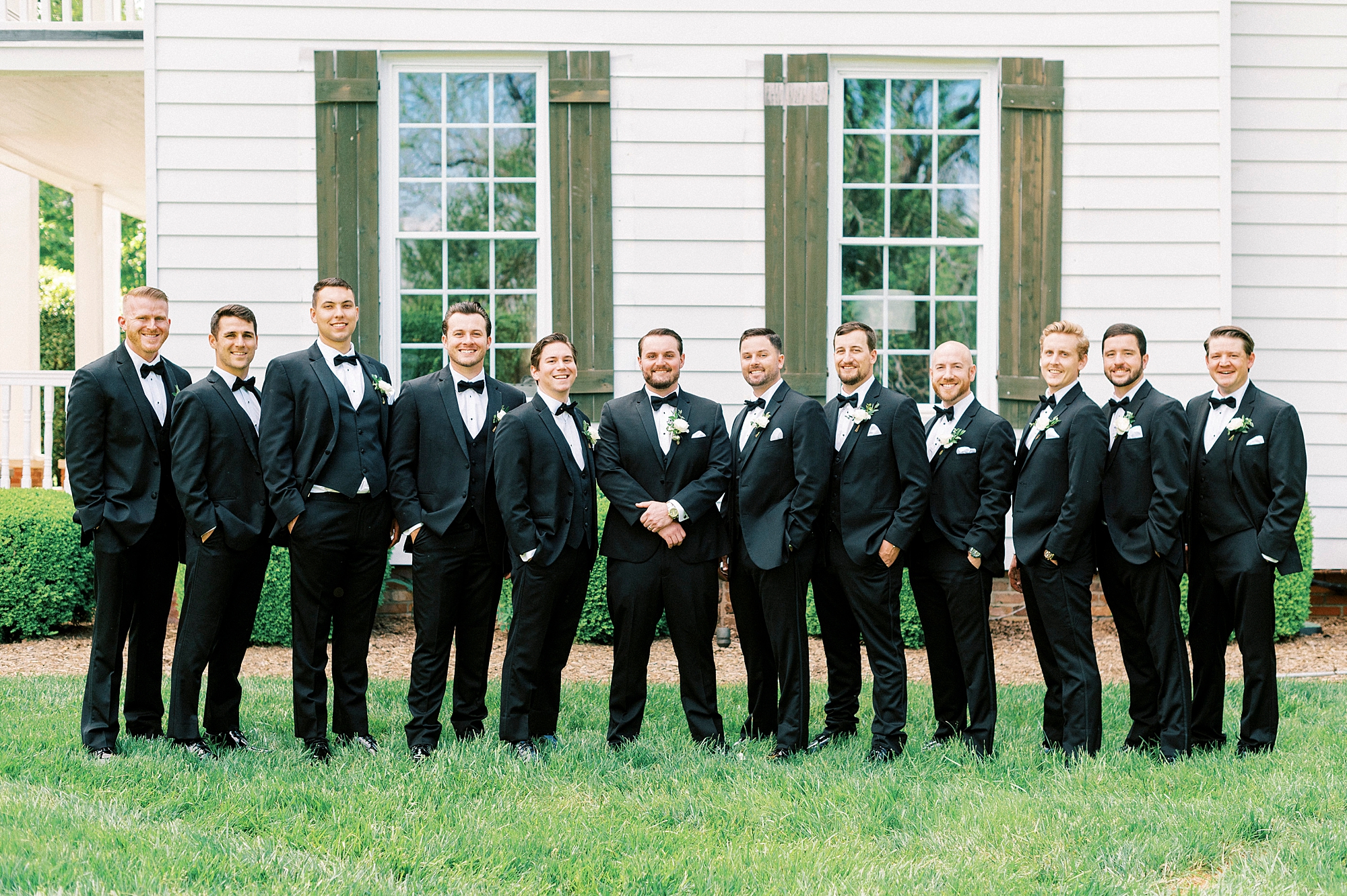 groom and groomsmen in black tuxes stand in a line outside the Venues at Langtree