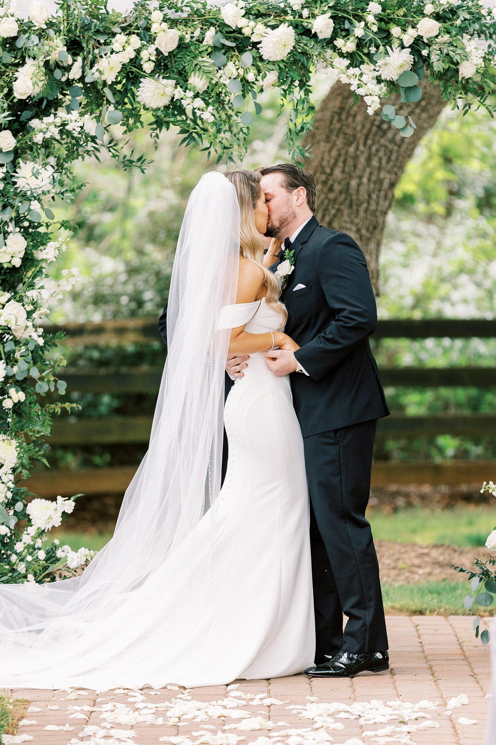 bride and groom kiss under arbor covered in white flowers at the Venues at Langtree
