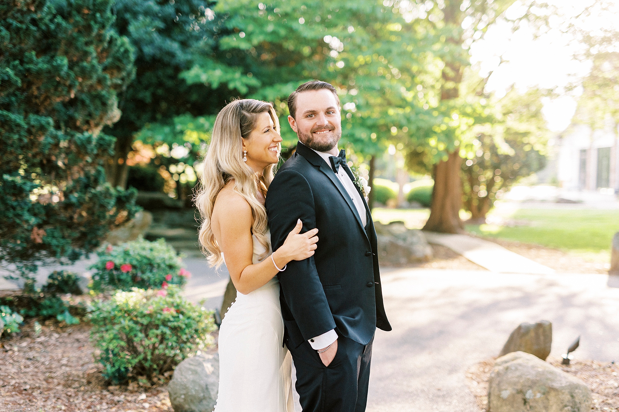 bride stands behind groom on brick pathway at the Venues at Langtree