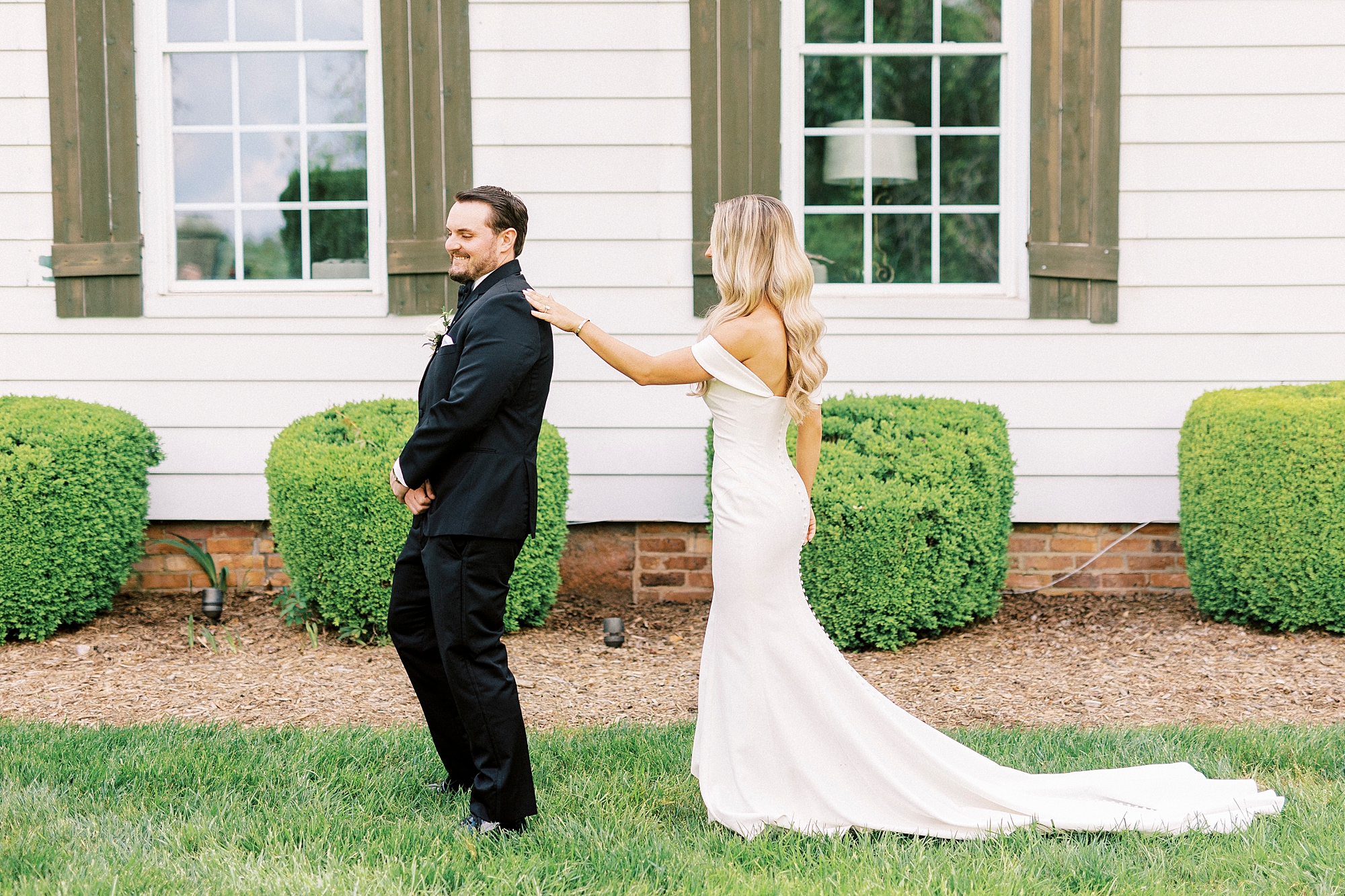 blonde woman reaches to tap groom's shoulder during first look at the Venues at Langtree