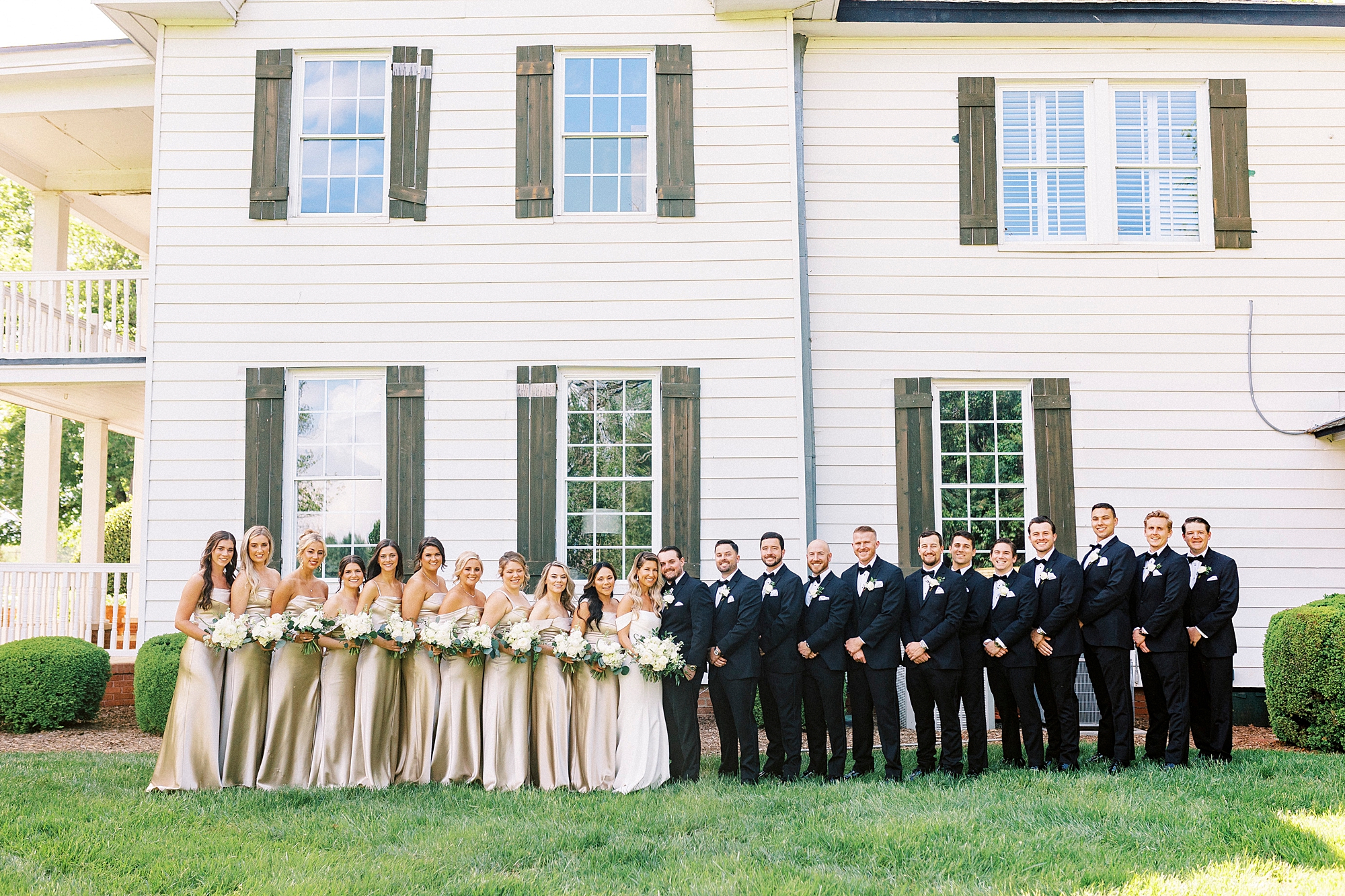 bride and groom pose with large wedding party outside the Venues at Langtree