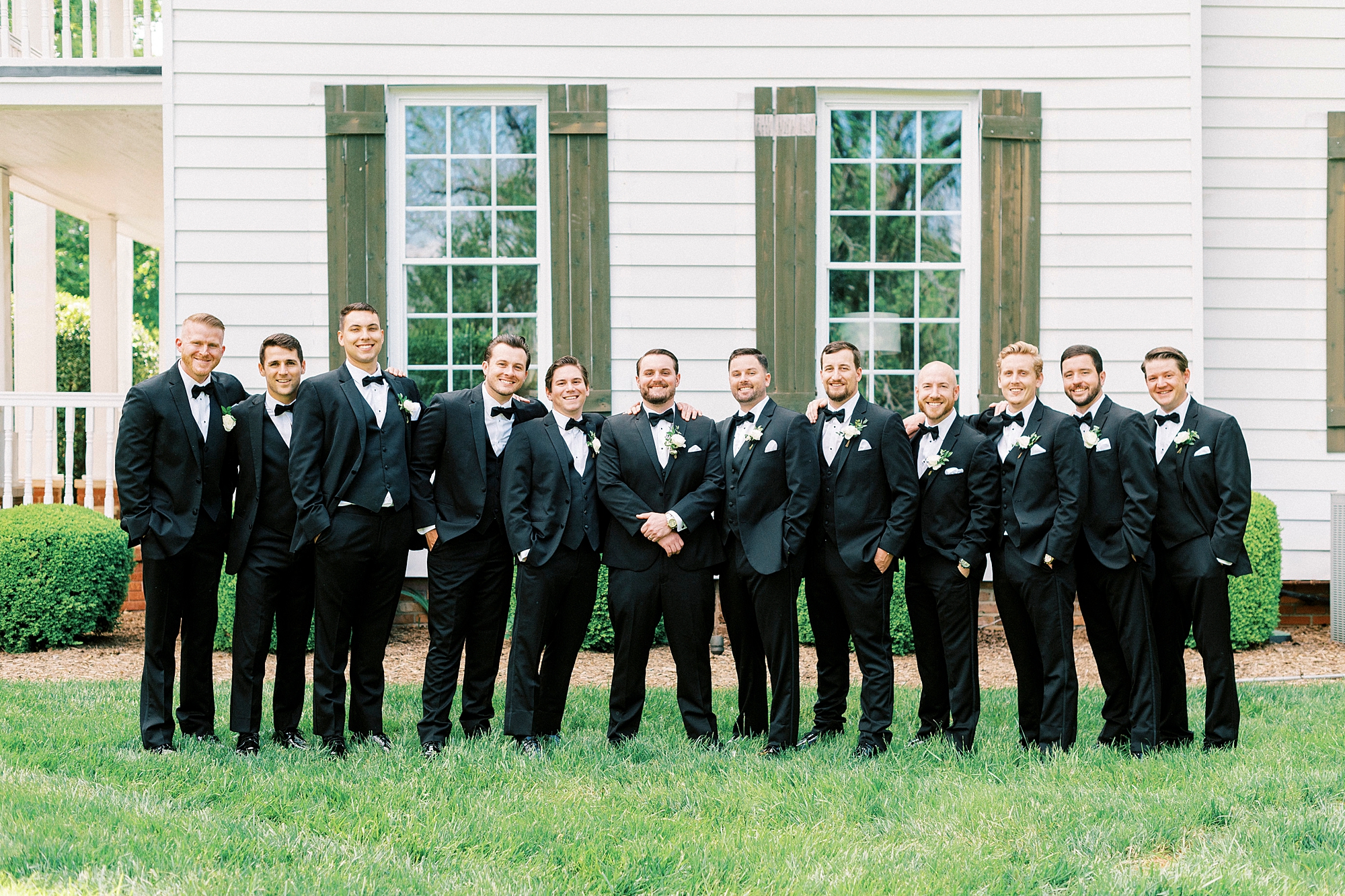groom stands with groomsmen in black suits outside the Venues at Langtree