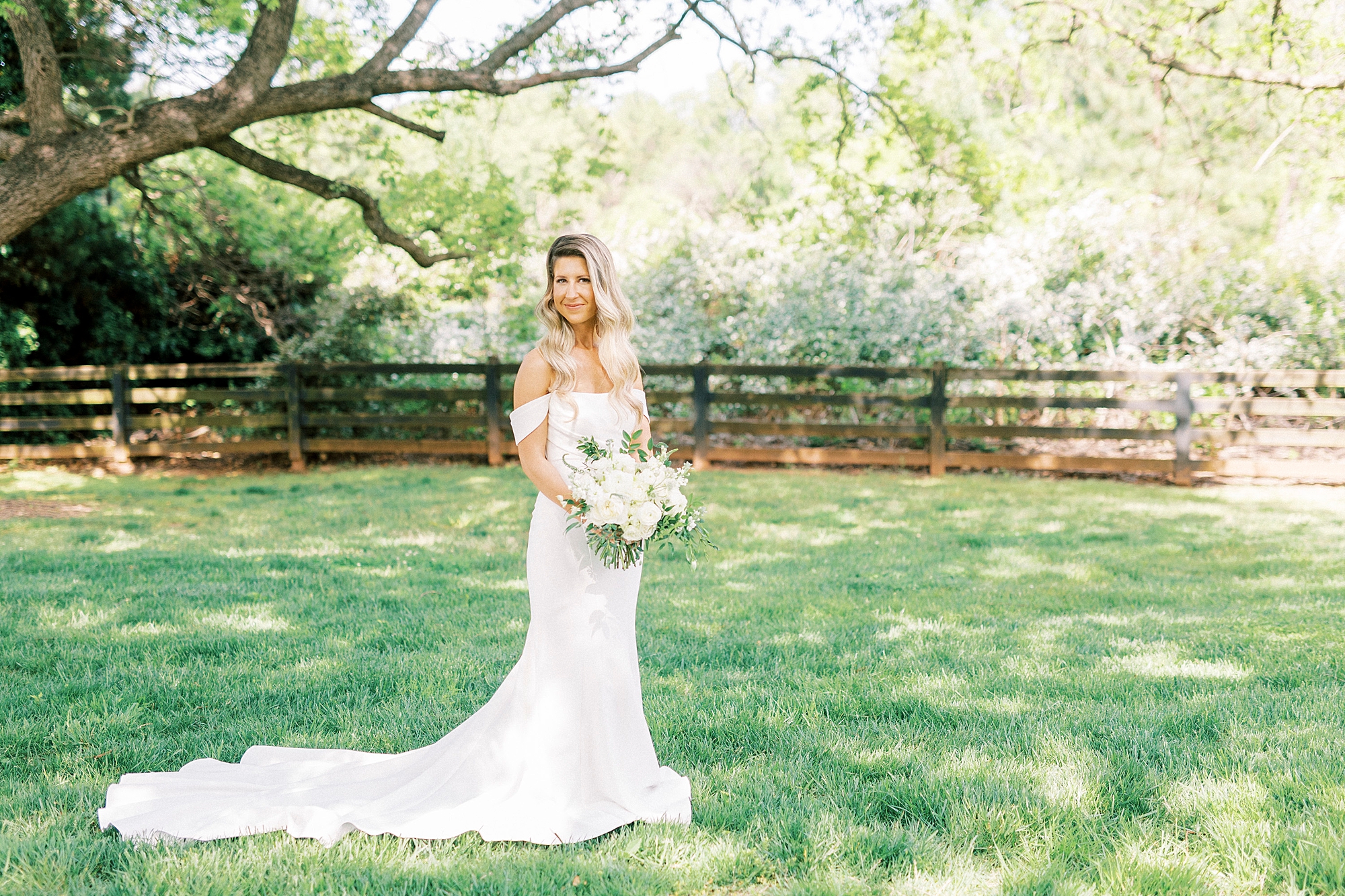 bride stands in field holding bouquet of white flowers at the Venues at Langtree