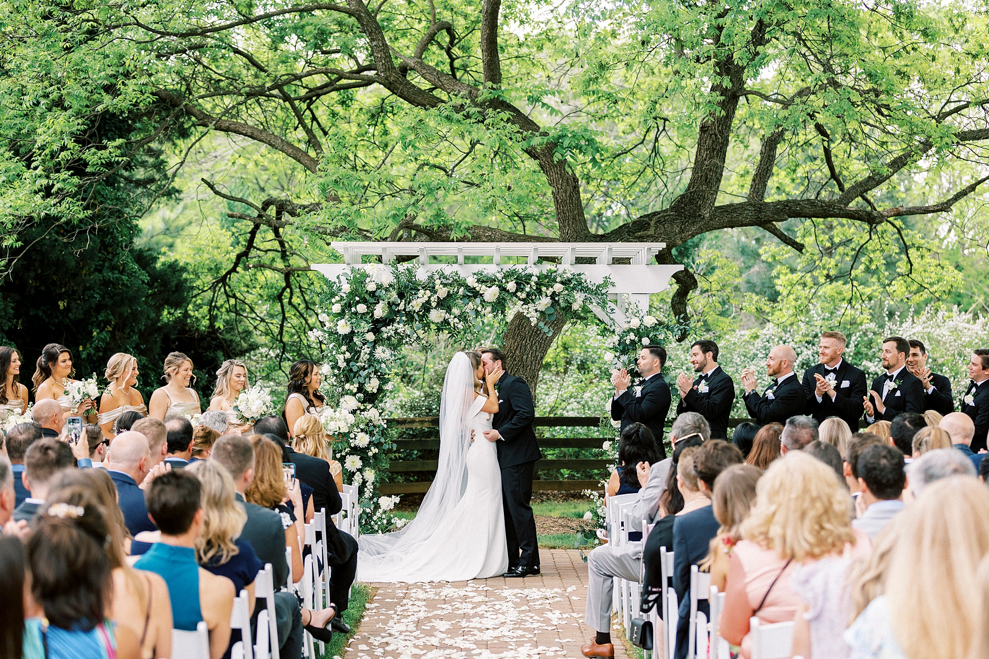 bride and groom kiss under white arbor with green and white florals at the Venues at Langtree