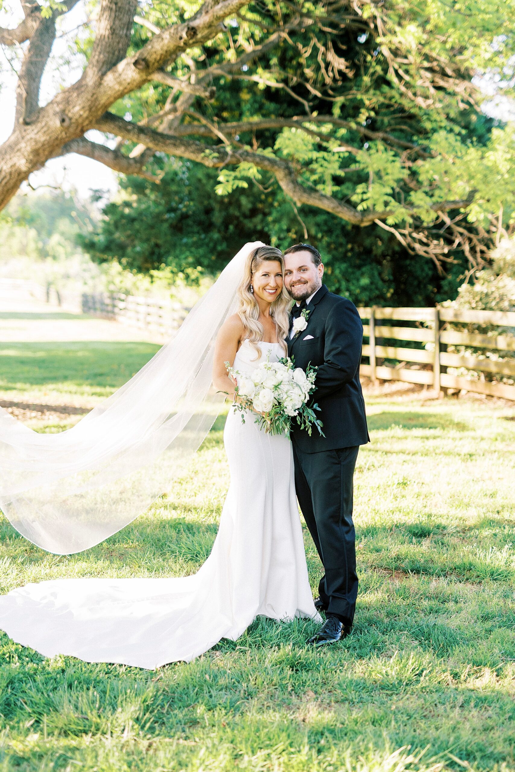 bride and groom hug with bride's veil floating behind them on lawn at the Venues at Langtree