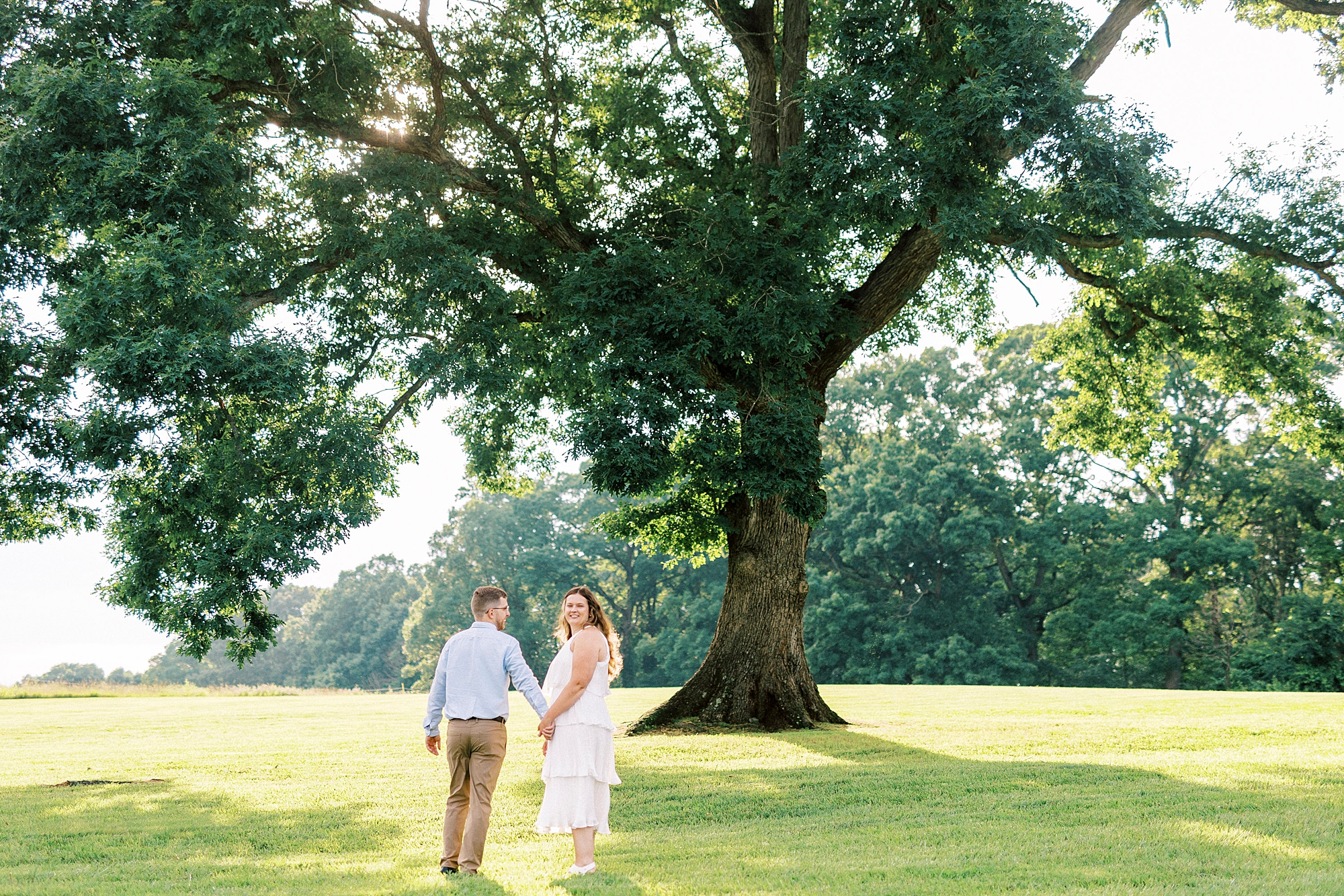 bride and groom hold hands walking under oak tree at Summerfield Farms