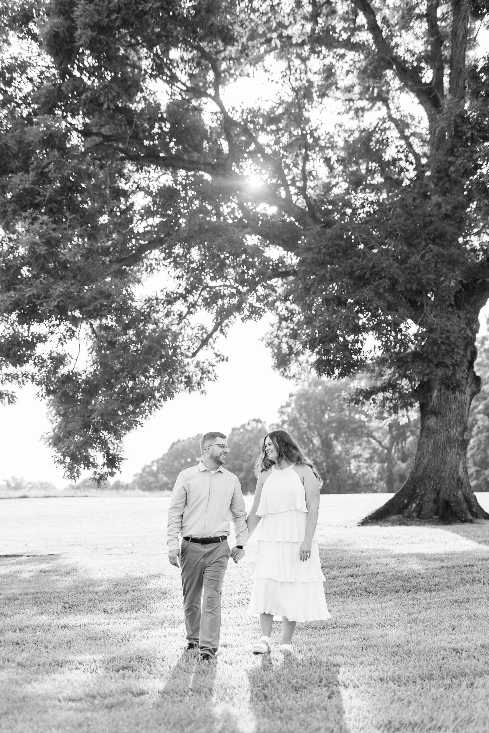 engaged couple holds hands walking away from tree at Summerfield Farms