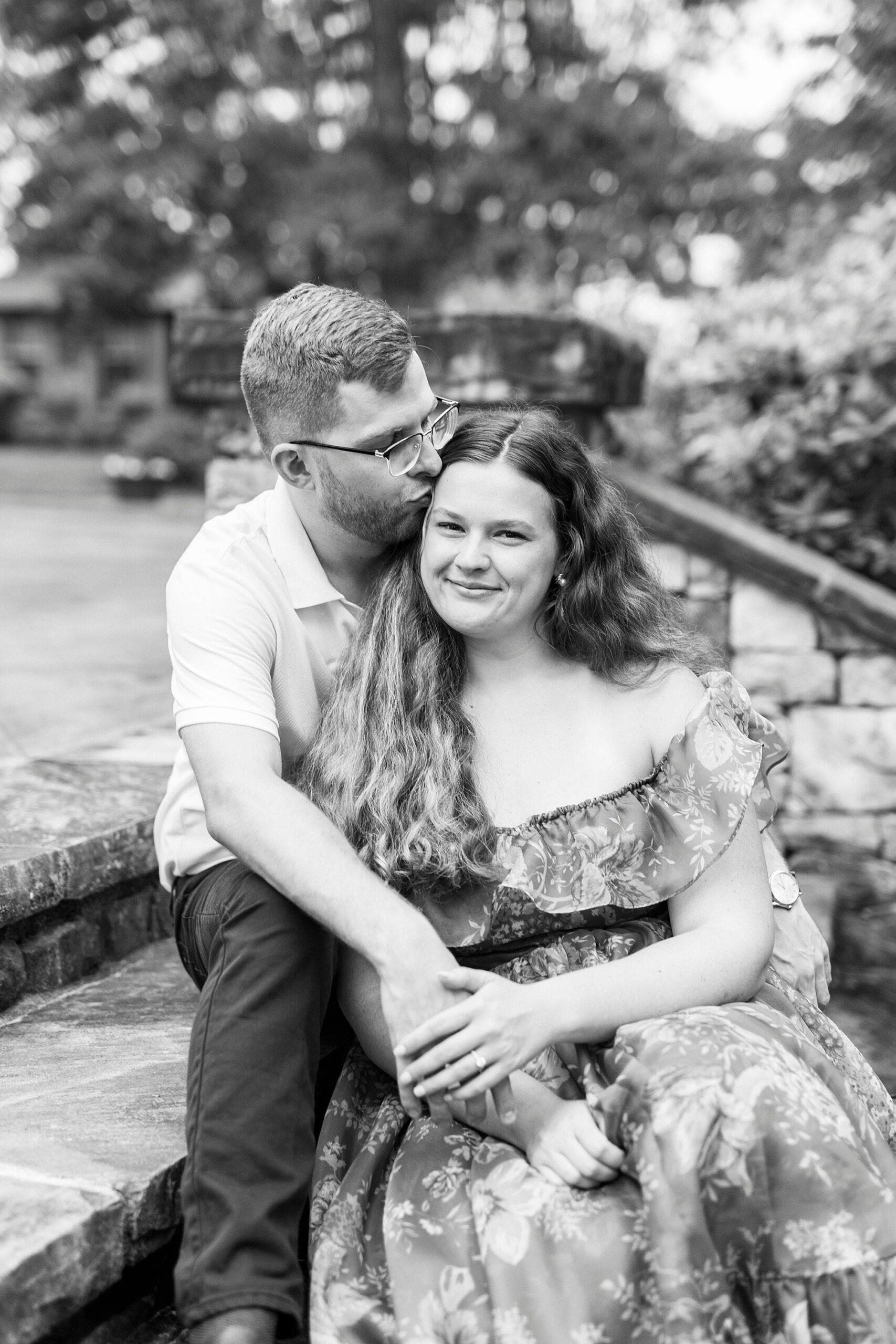 man sits on steps with woman between his knees on a step below kissing her forehead