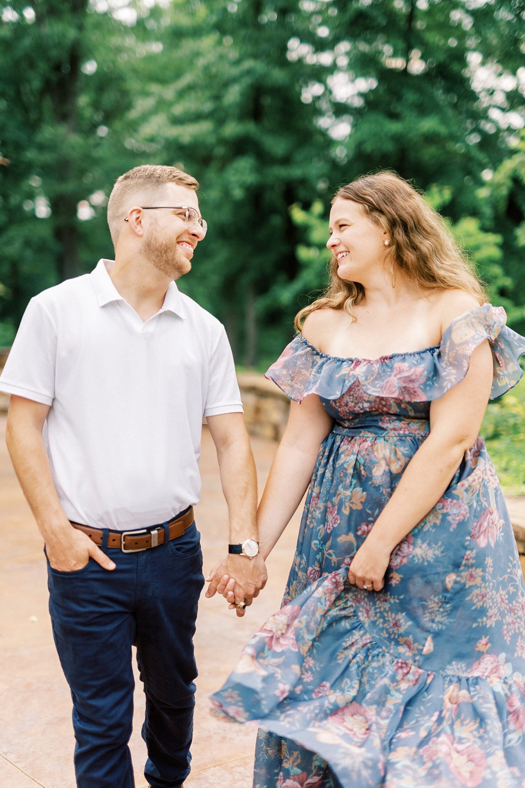 engaged couple holds hands walking across brick patio at Summerfield Farms